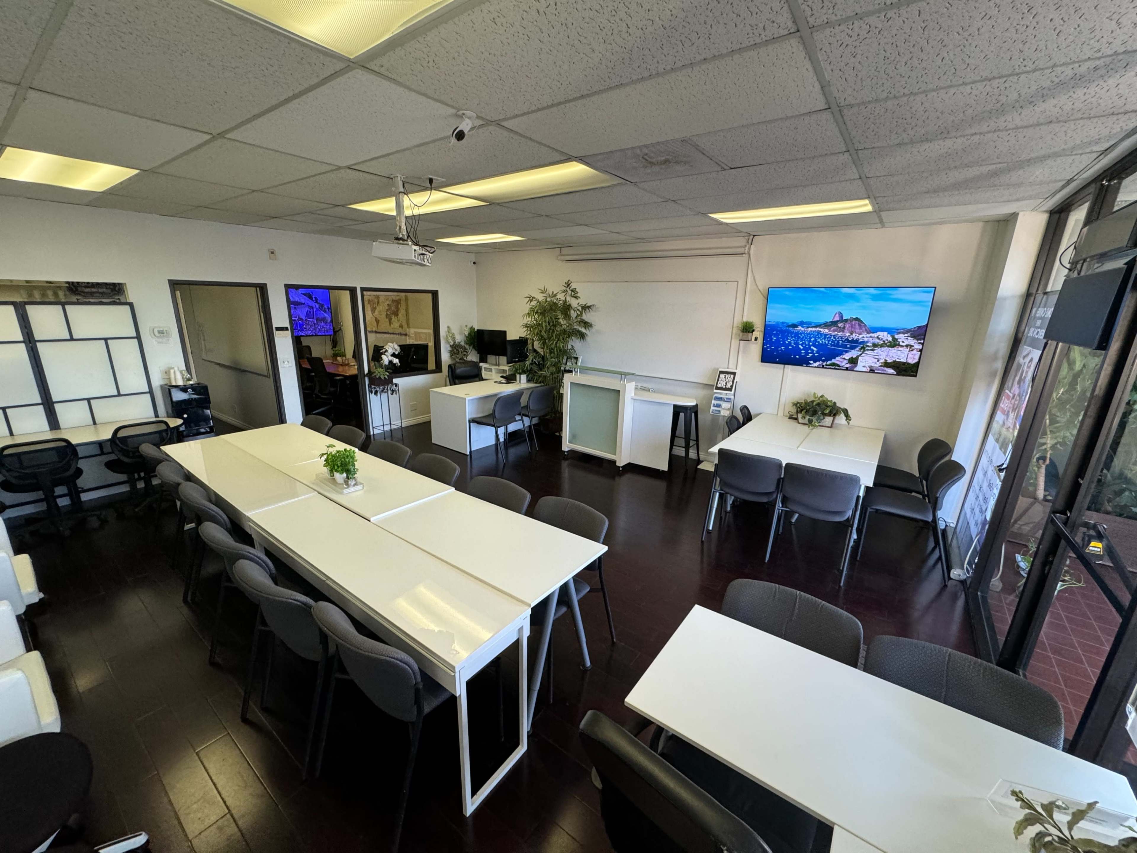 A spacious office interior with white tables, gray chairs, and a large television mounted on the wall.