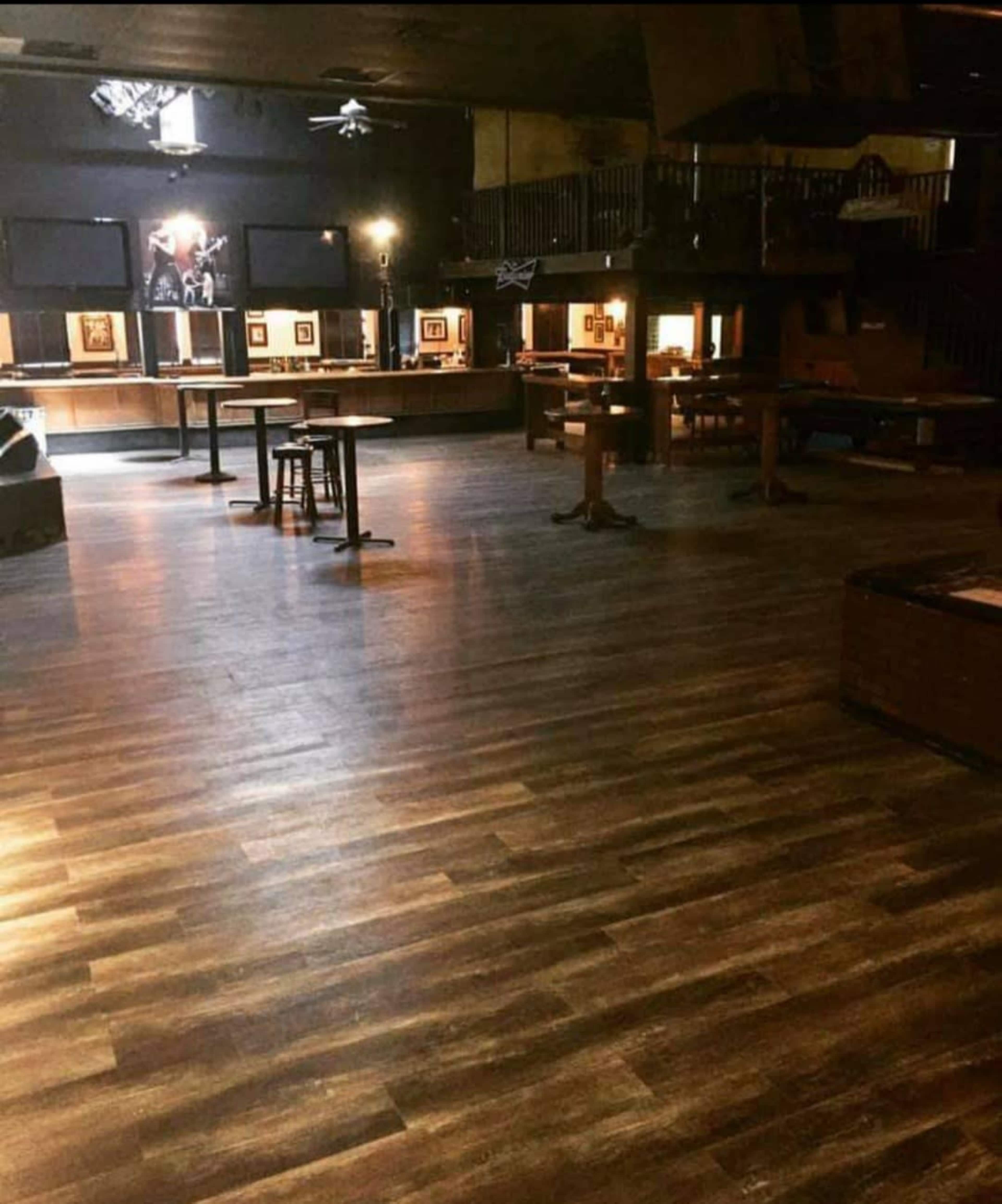 A dimly lit interior of a music venue with polished wooden flooring and empty tables and chairs arranged throughout.