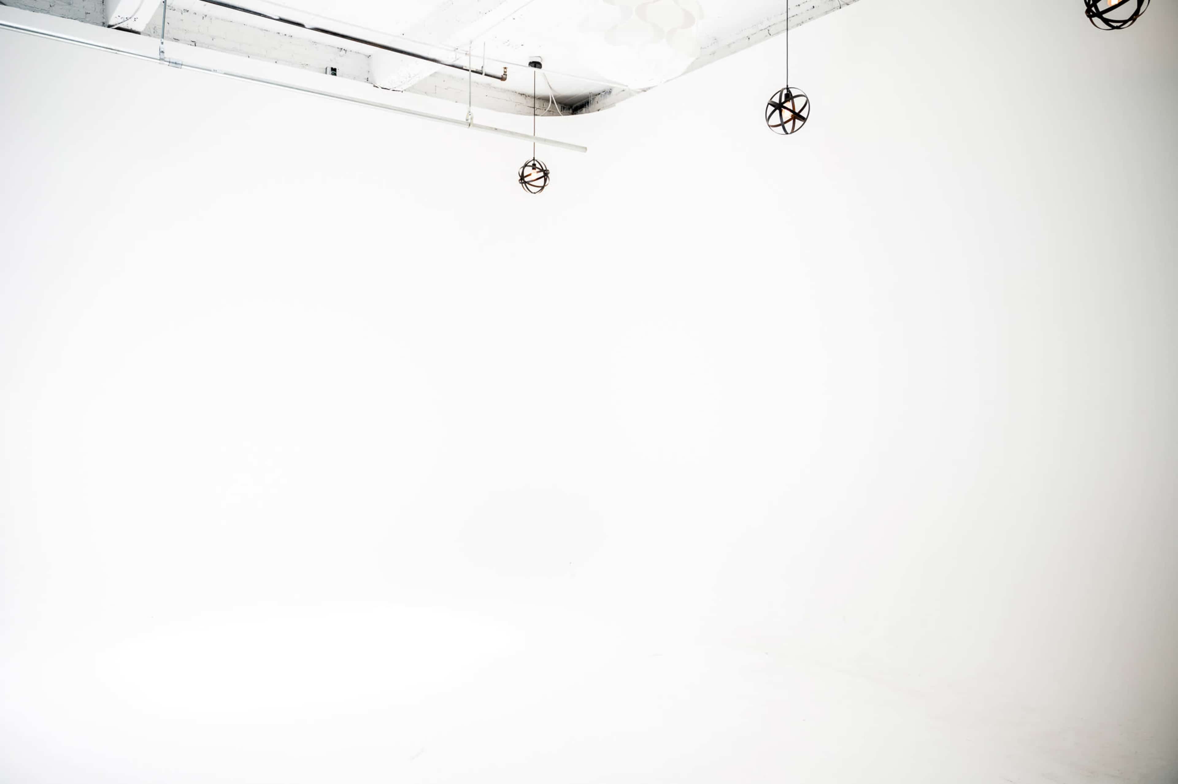 The image features a minimalist studio space with a white background and three pendant lights hanging from the ceiling.