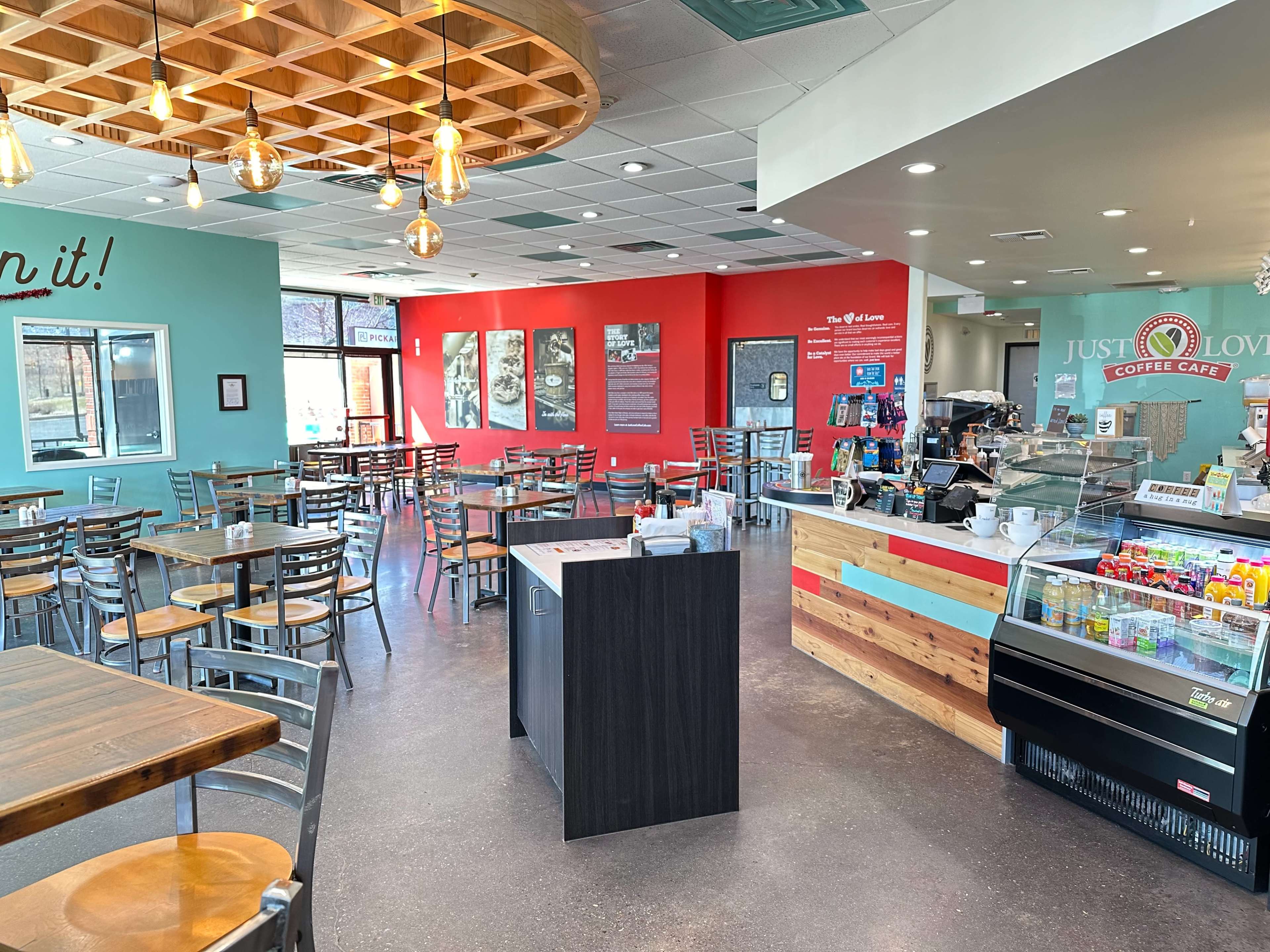 A cozy coffee shop featuring a mix of wooden tables and metal chairs, with a service counter displaying a selection of beverages and pastries.