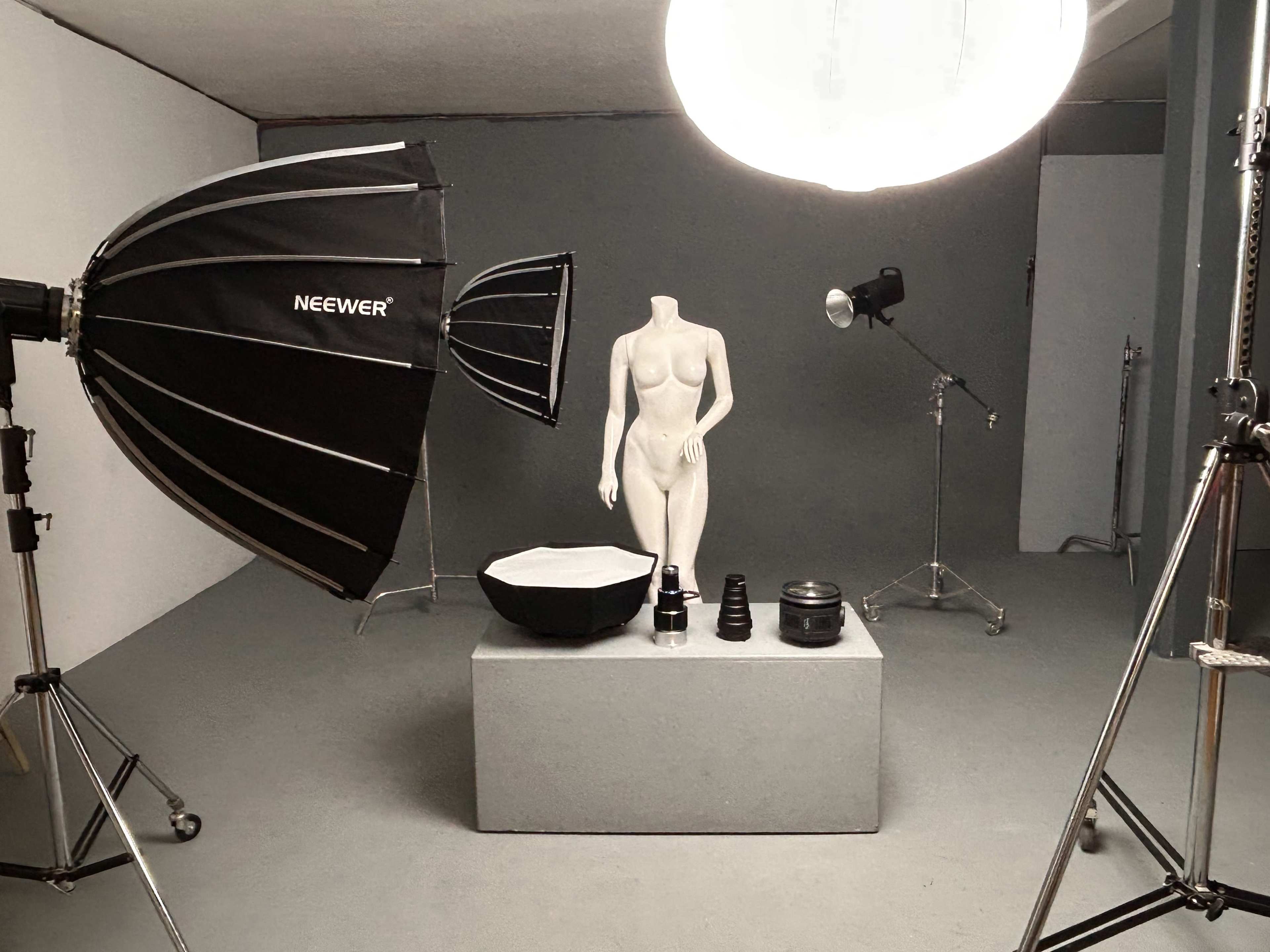 The image shows a photography studio setup featuring a mannequin on a pedestal, multiple softbox lights, and camera equipment arranged on a gray backdrop.