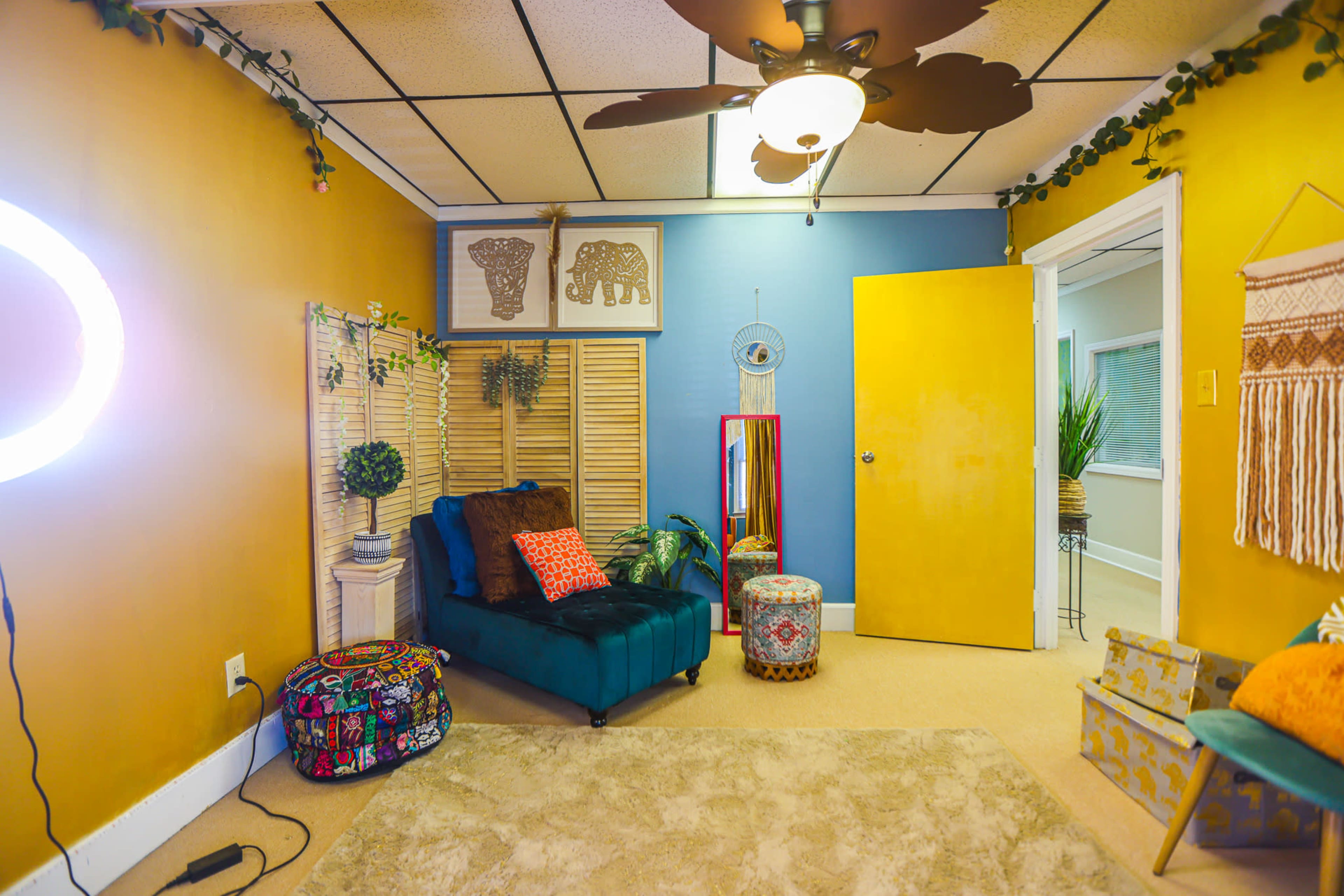 The room features a blue and yellow color scheme, a black couch, a small table, and decorative elements like plants and art.