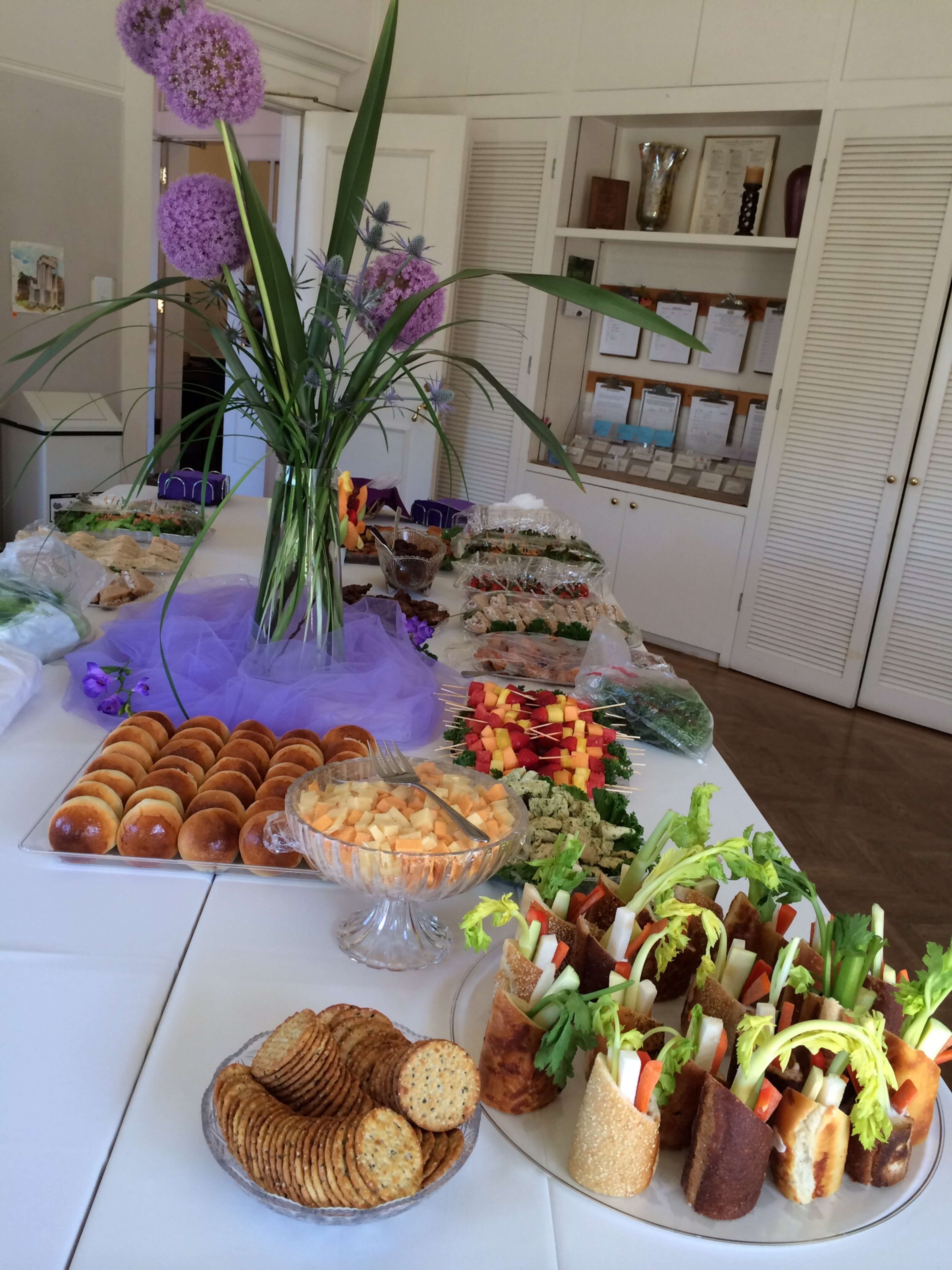 A buffet table adorned with a variety of colorful food items, including sandwiches, fruits, vegetables, and pastries, arranged neatly with a floral centerpiece.