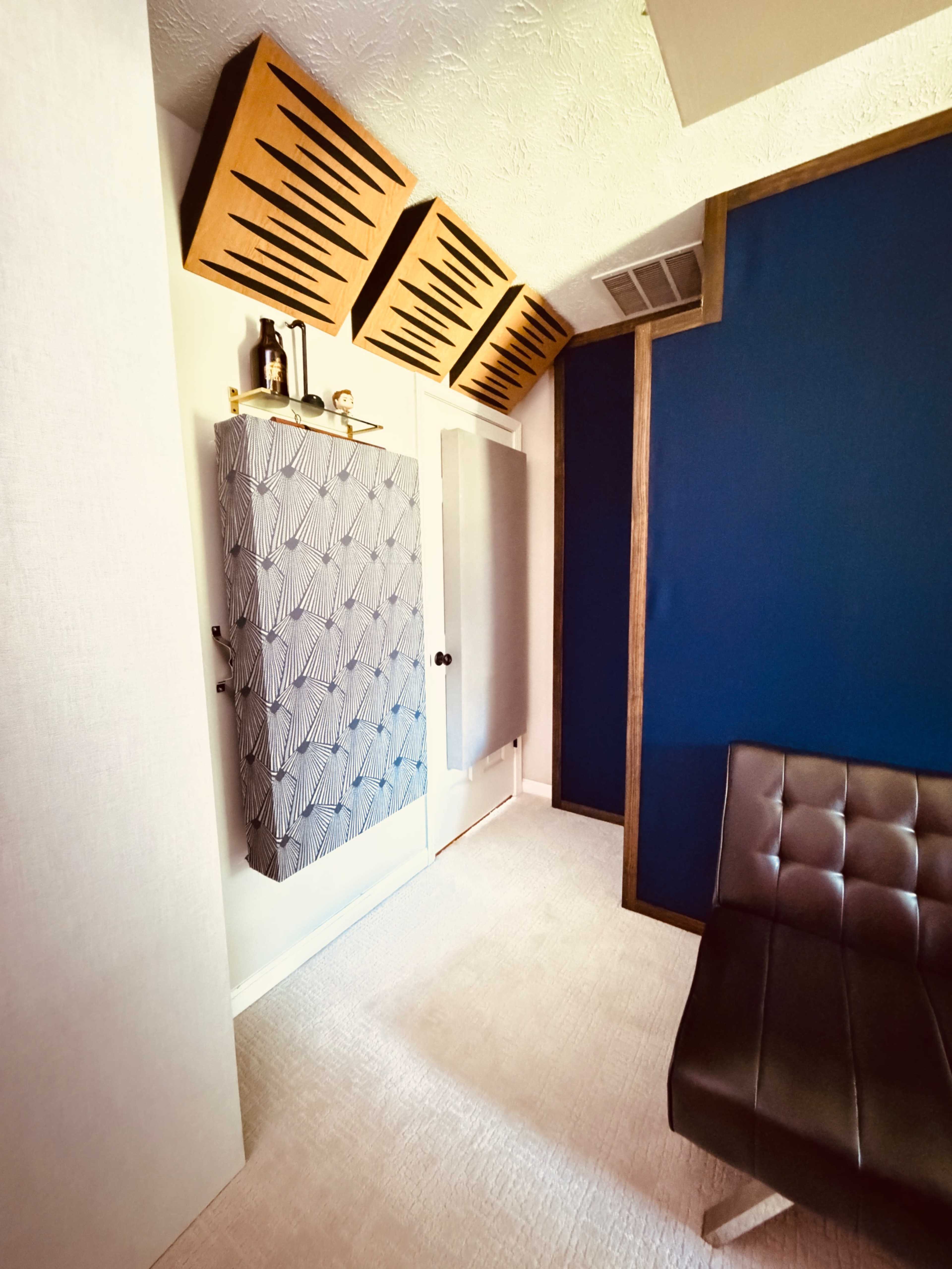 The image shows a room with a blue accent wall, an upholstered black chair, and soundproof panels mounted on the ceiling.