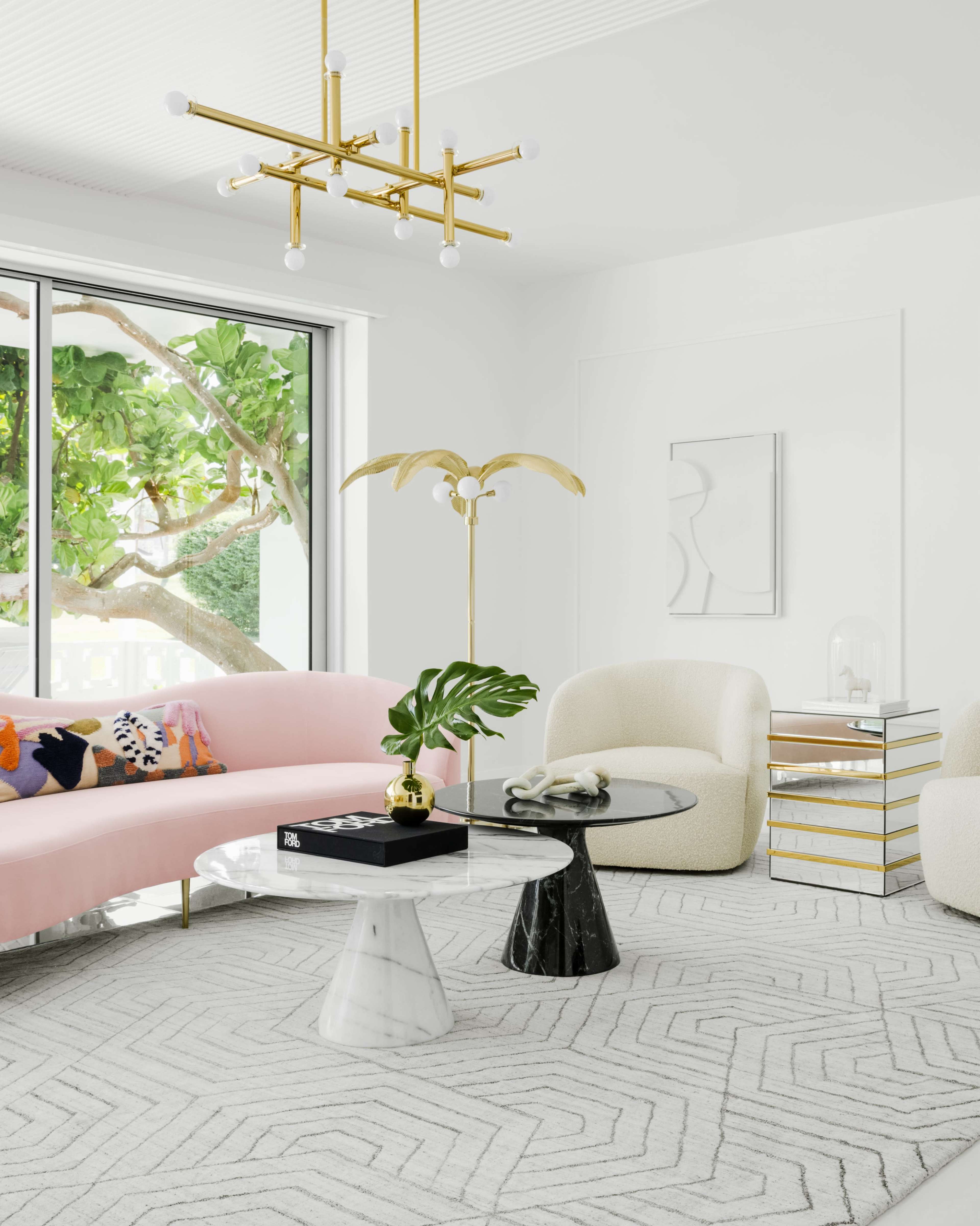 A modern living room features a pink sofa, marble and black tables, a decorative floor lamp, and large windows with a view of greenery.