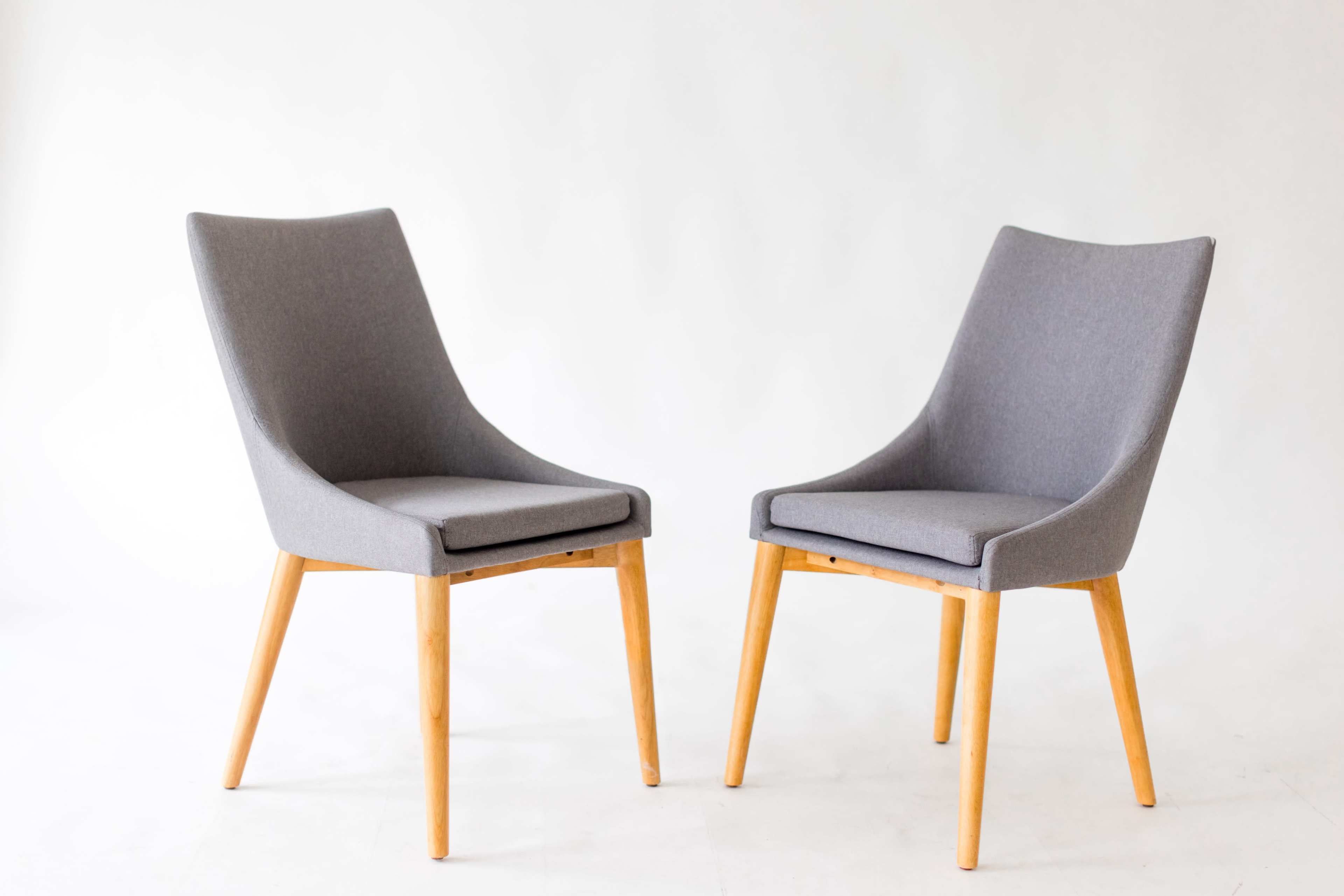 Two gray upholstered chairs with wooden legs are positioned facing each other on a plain background.