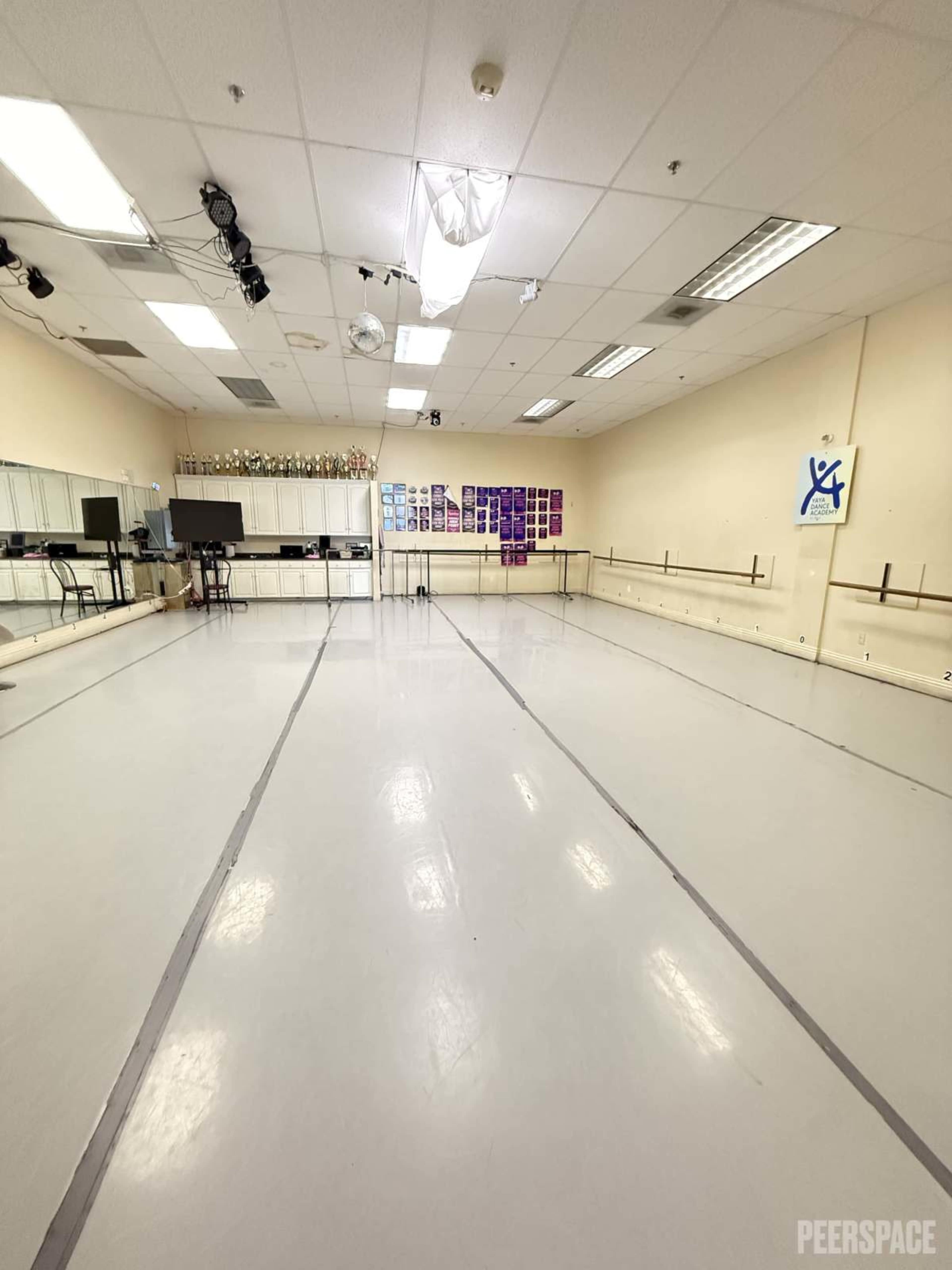 The image shows a spacious dance studio with mirrored walls, wooden ballet barres, and a clean, white floor.