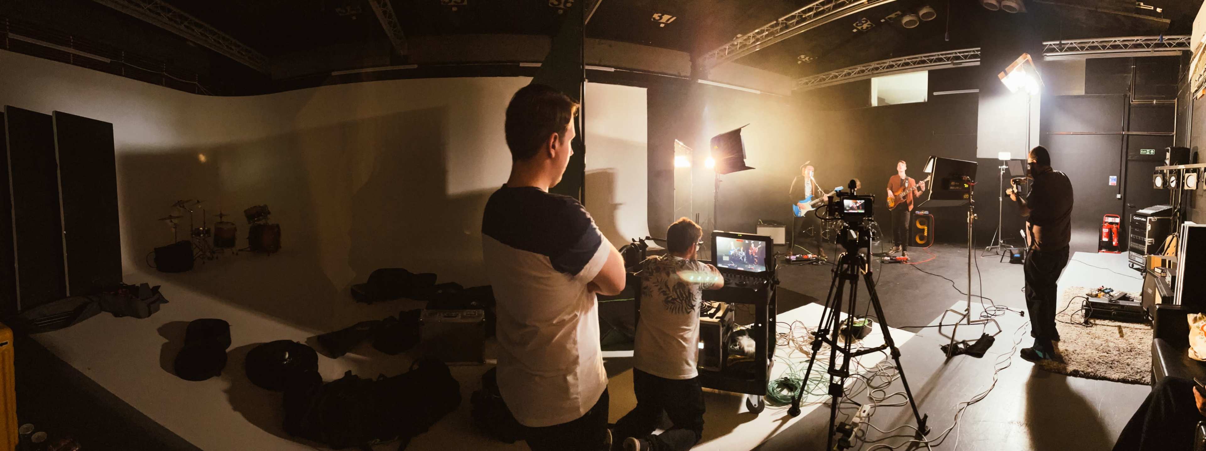 A band performs in a studio while a crew operates cameras and monitors nearby.