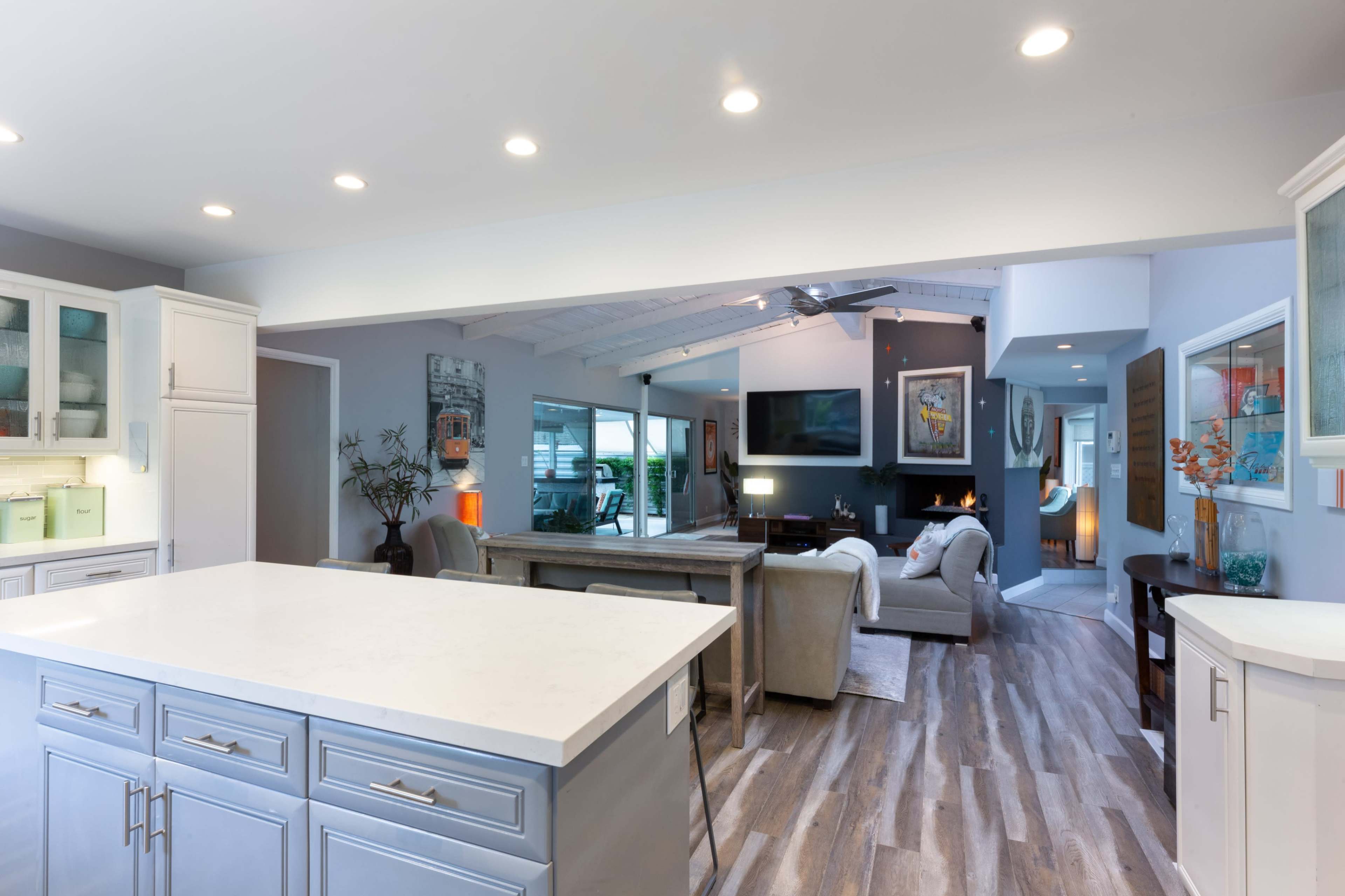 A modern open-concept living space features a kitchen island, dining area, and a cozy seating area with a fireplace, all adorned with neutral tones and natural light.