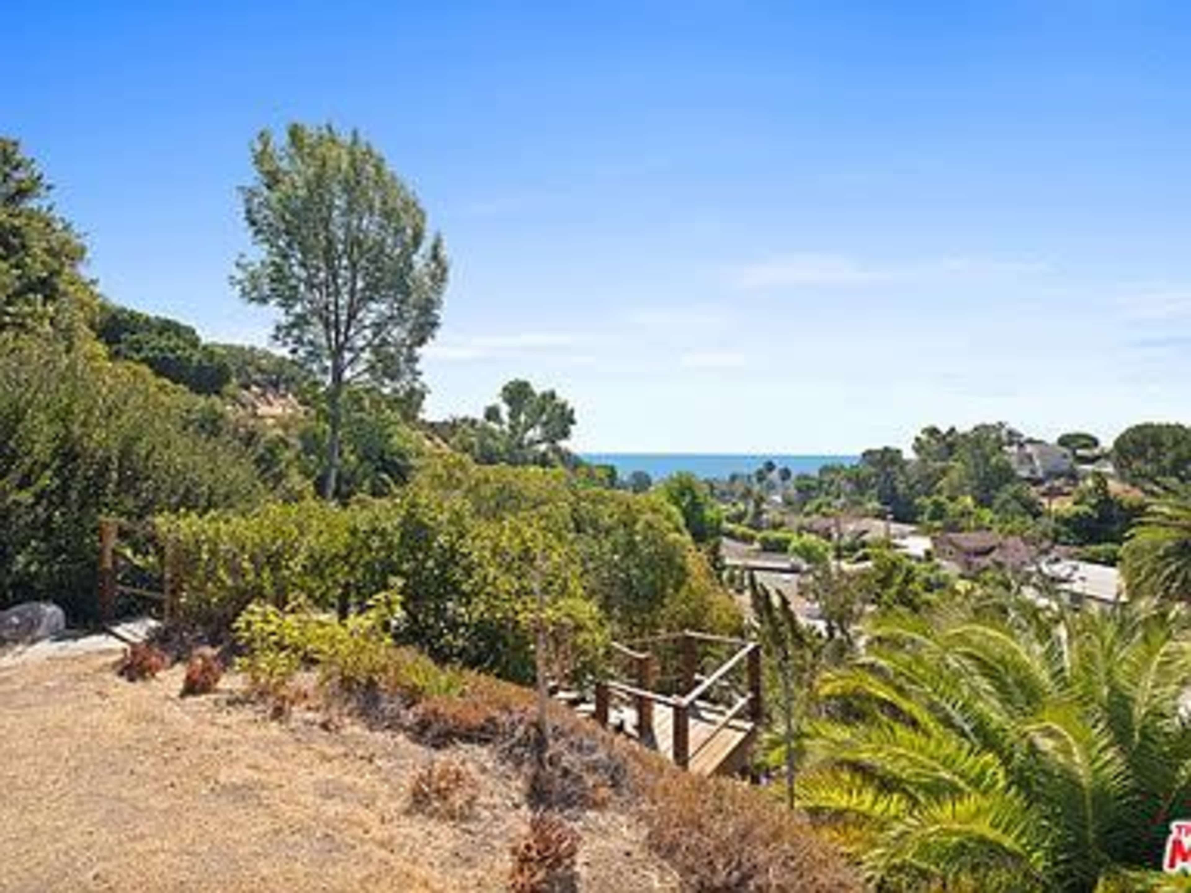 The image shows a coastal landscape with trees, shrubs, and a view of the ocean in the background.