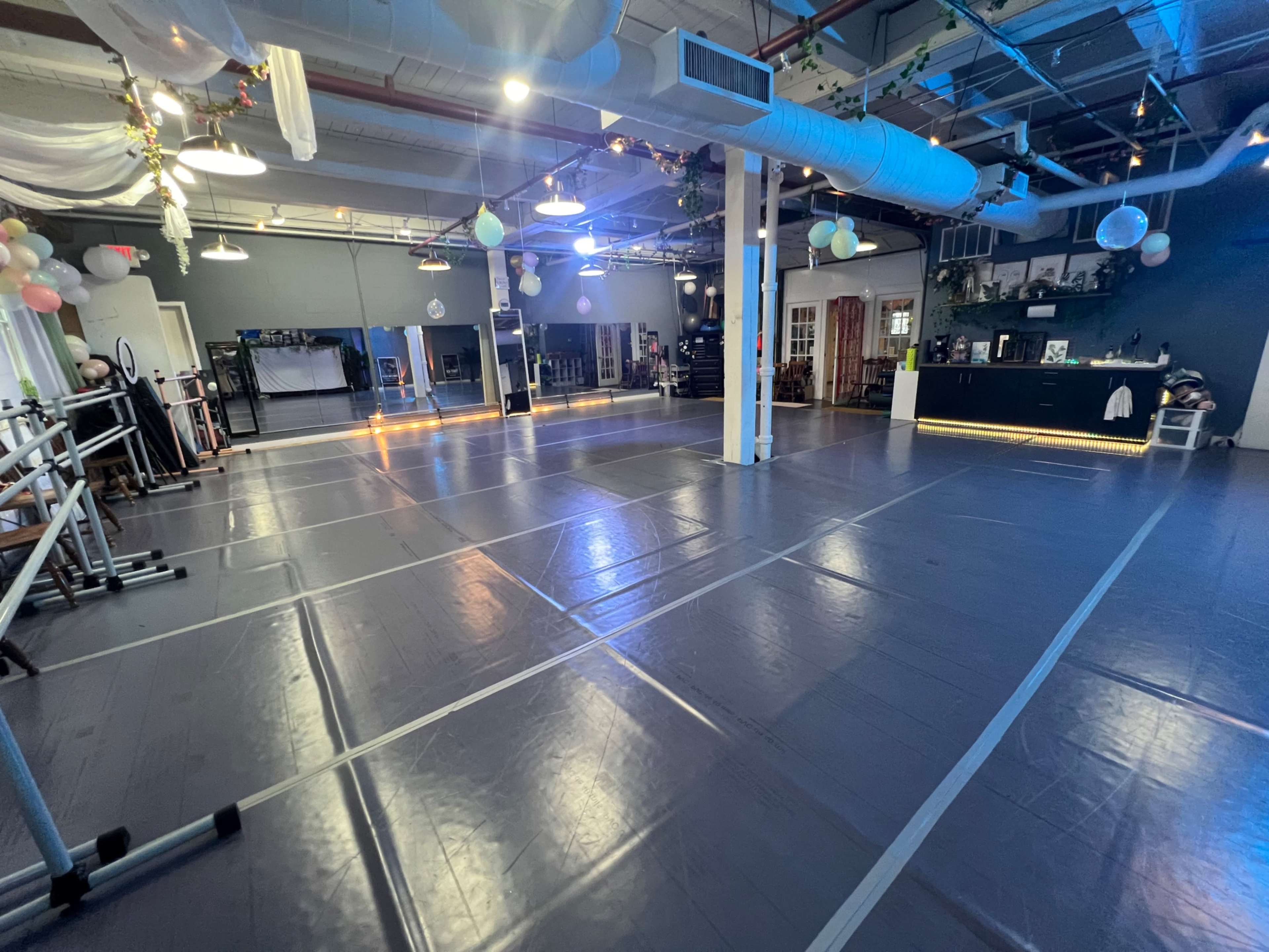 A spacious dance studio with a mirrored wall, ballet bars, and overhead lighting.
