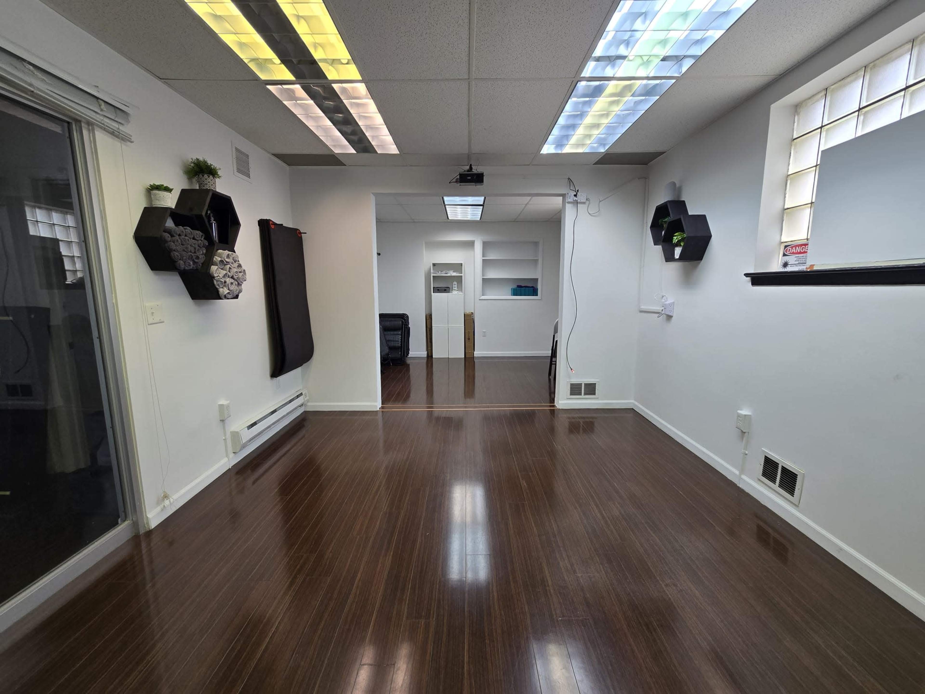 A spacious, well-lit room with polished wooden floors, a few decorative wall-mounted shelves, and a glass door leading to another area.