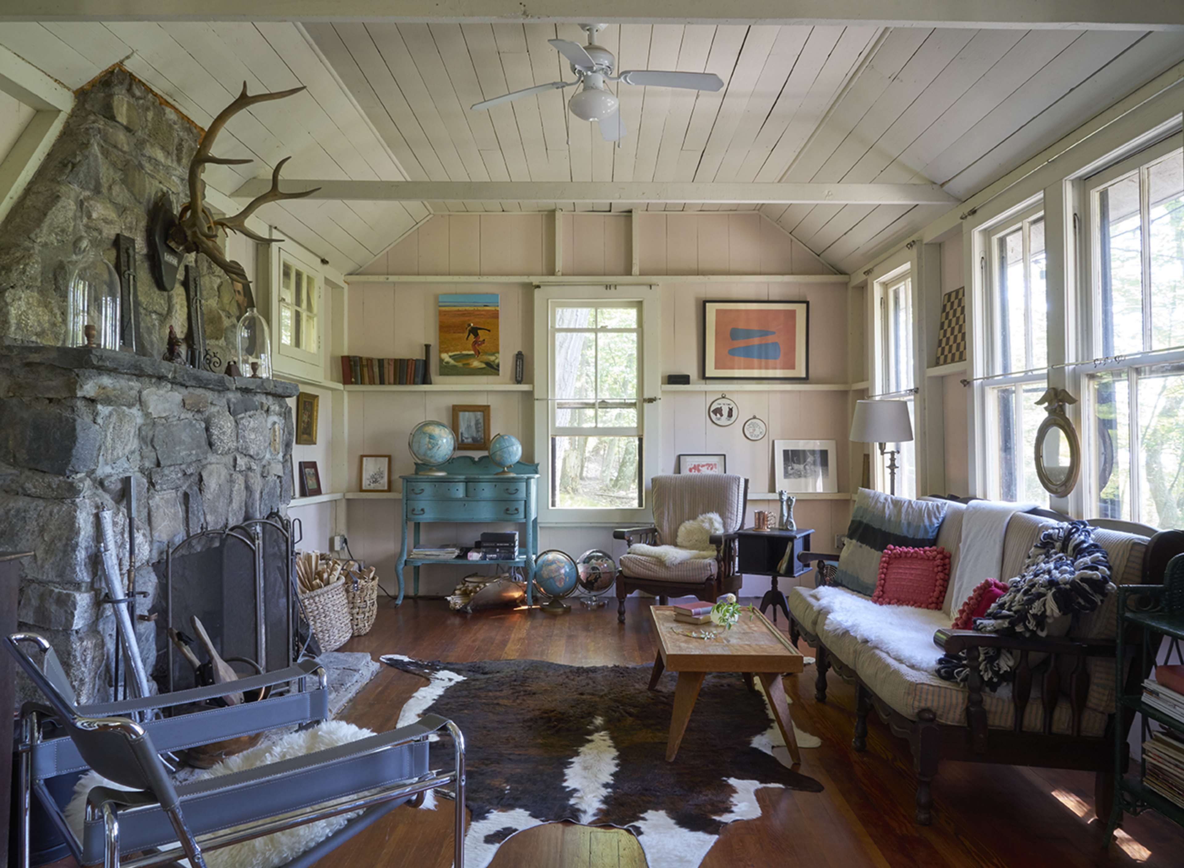 The living room features a stone fireplace, large windows, and a mix of comfortable furniture, including a sofa and armchairs, arranged around a wooden coffee table.