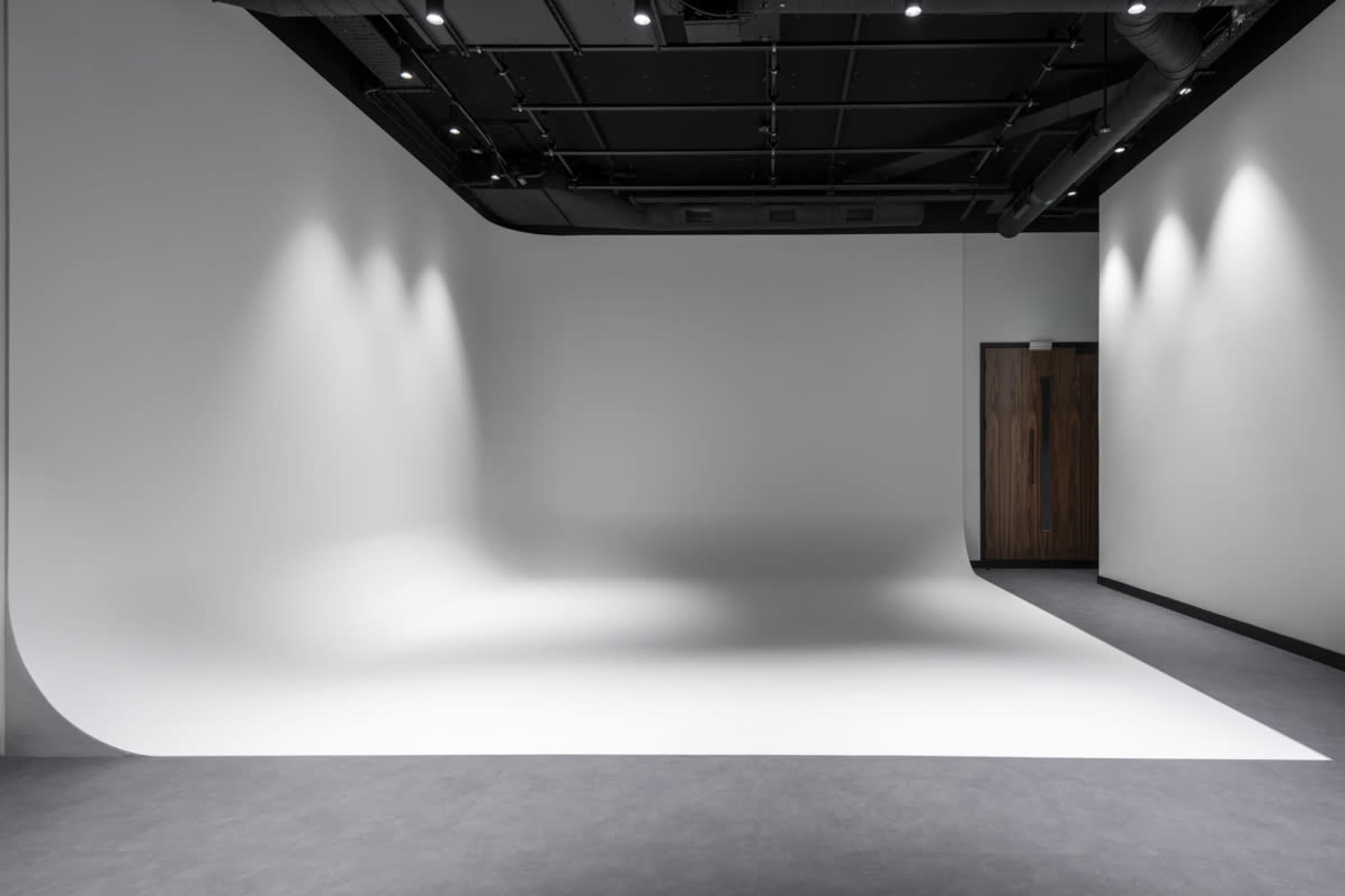 The image shows a minimalist photography studio with a seamless white backdrop and dimmed overhead lighting.