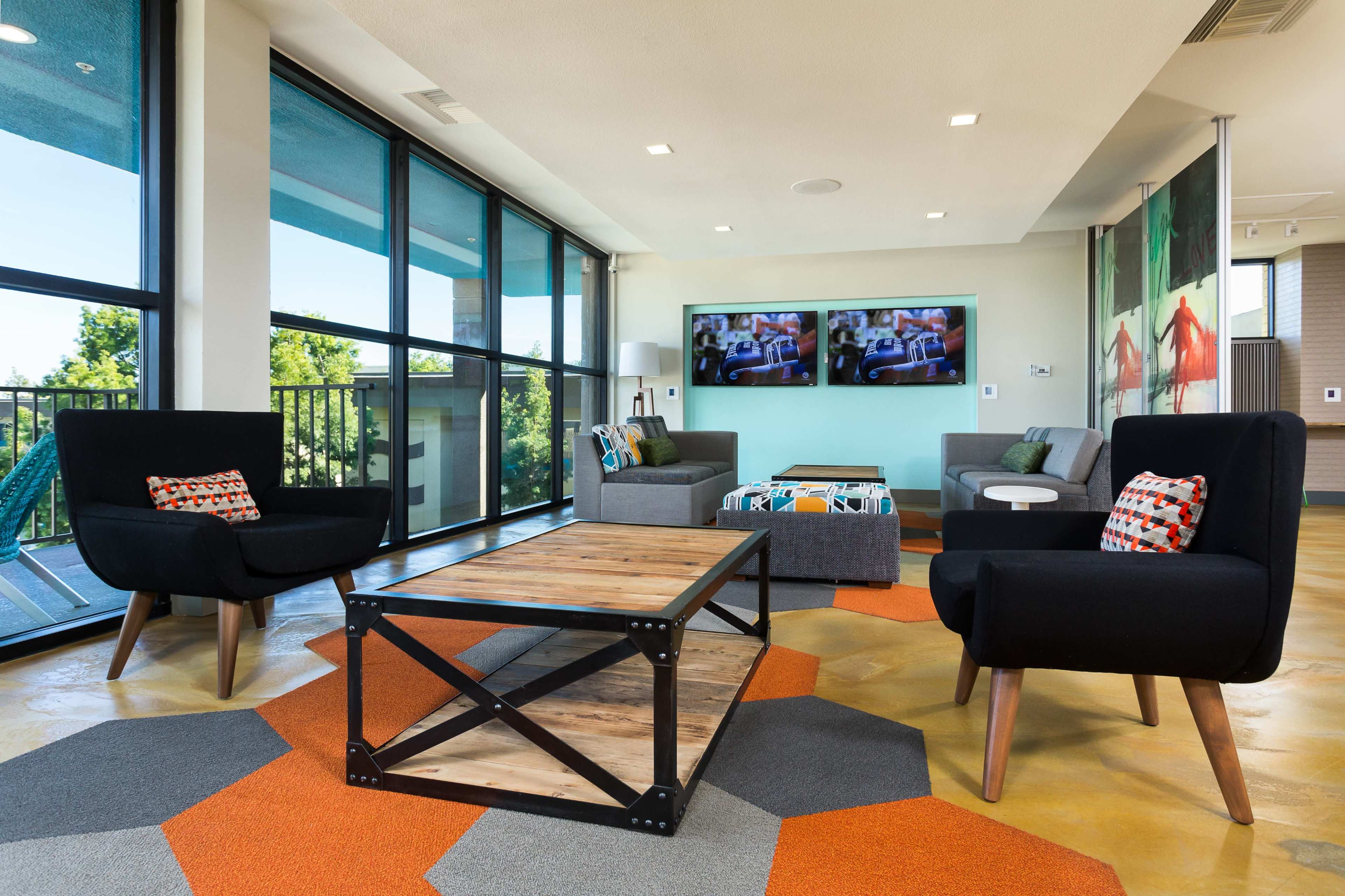 A modern lounge area with large windows, a coffee table, and various seating arrangements, including black armchairs and a gray sofa.