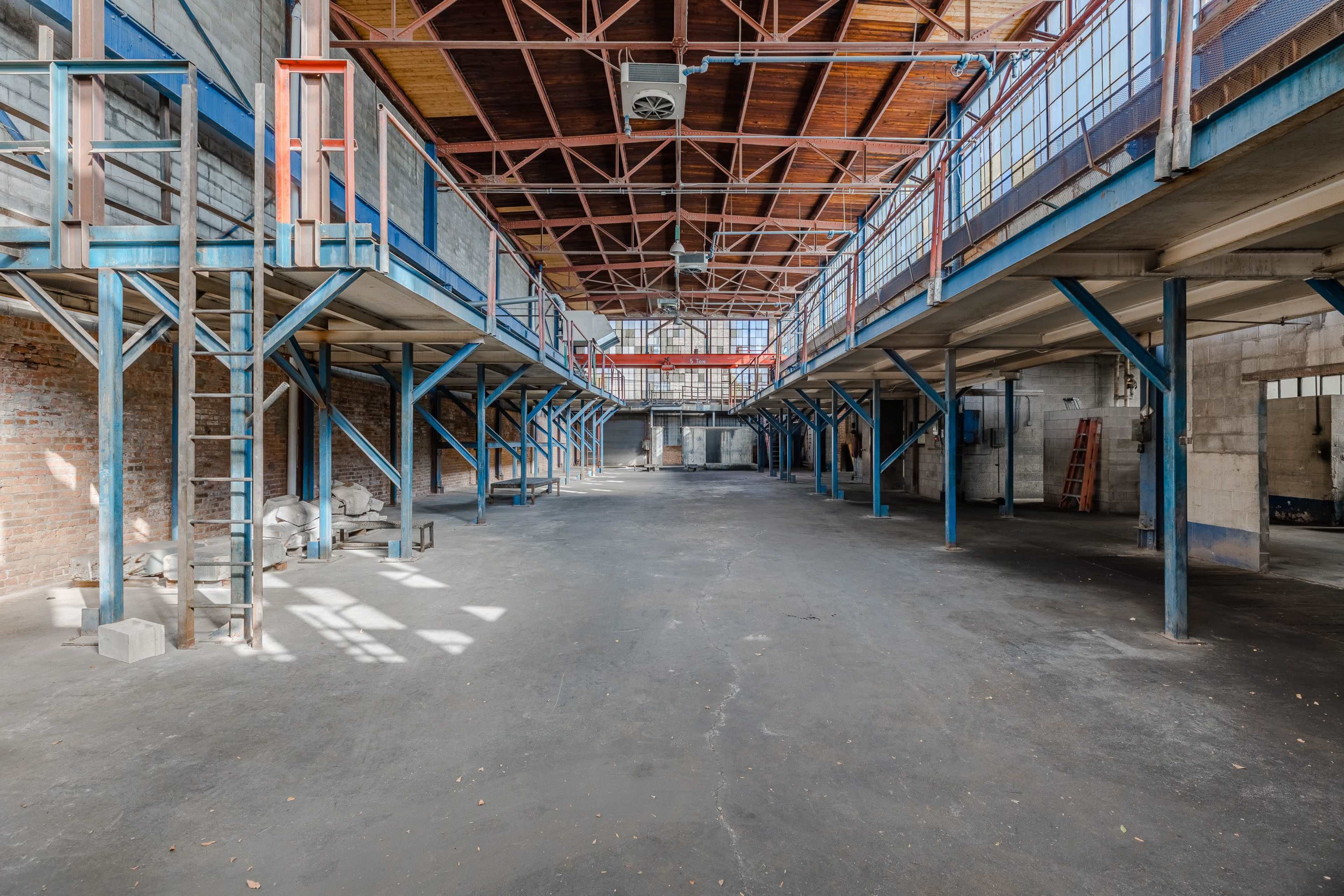 A large, vacant industrial space with metal support beams, elevated walkways, and a concrete floor.