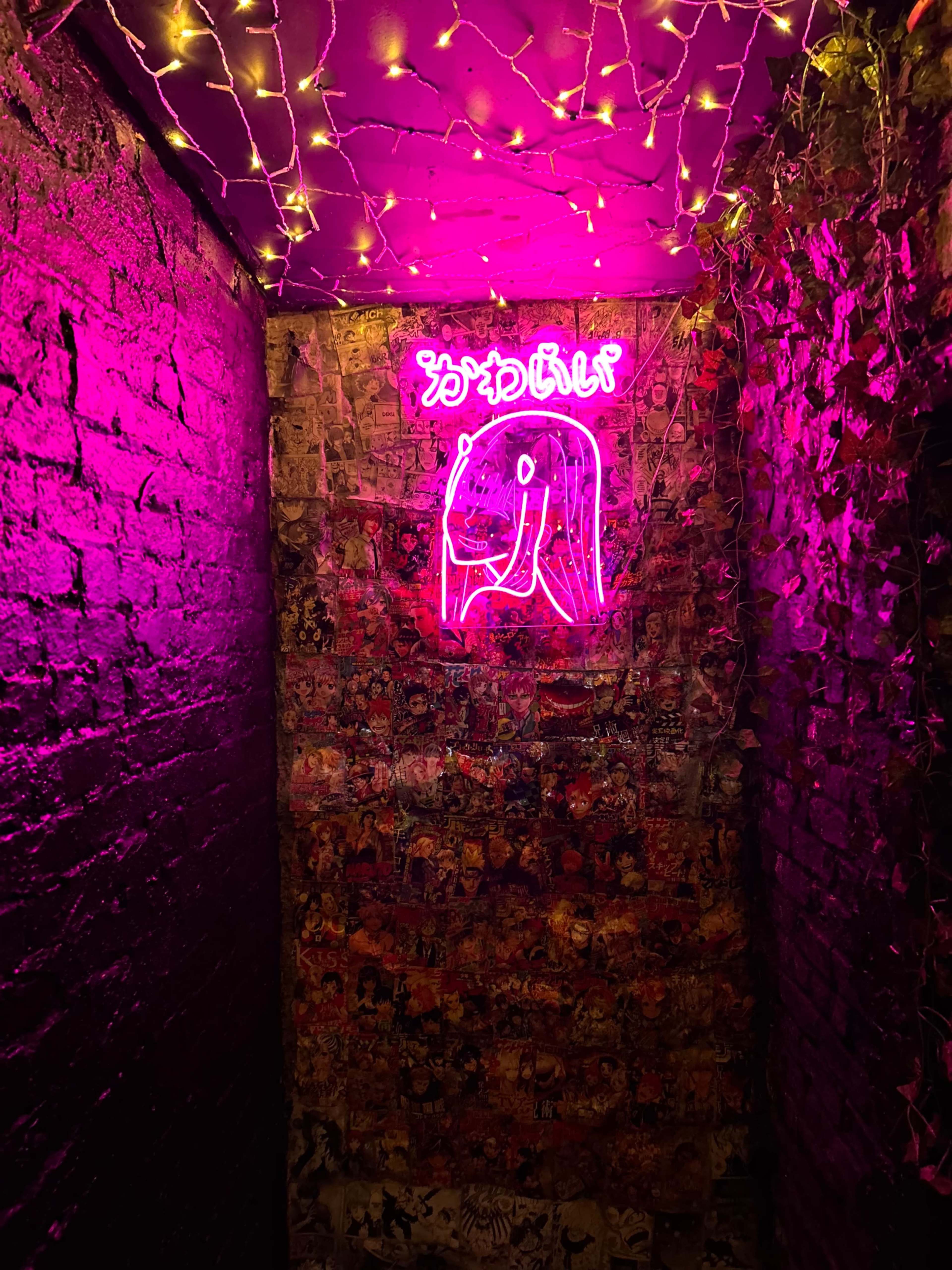 A dimly lit hallway with a pink neon sign and walls covered in colorful posters and decorations.