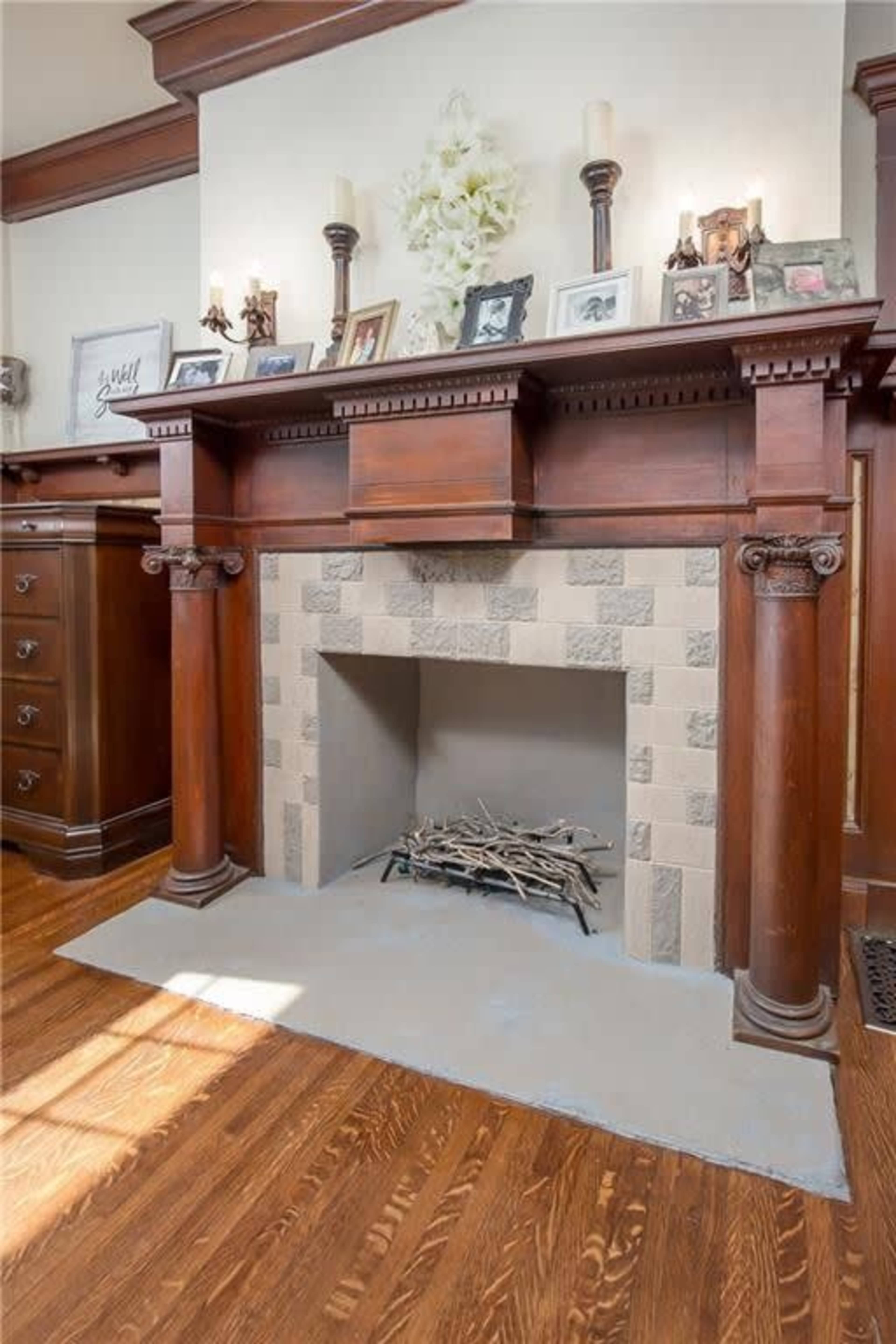 The image shows a wooden fireplace mantel with decorative photos and candles above a tiled firebox, complemented by a light gray hearth.