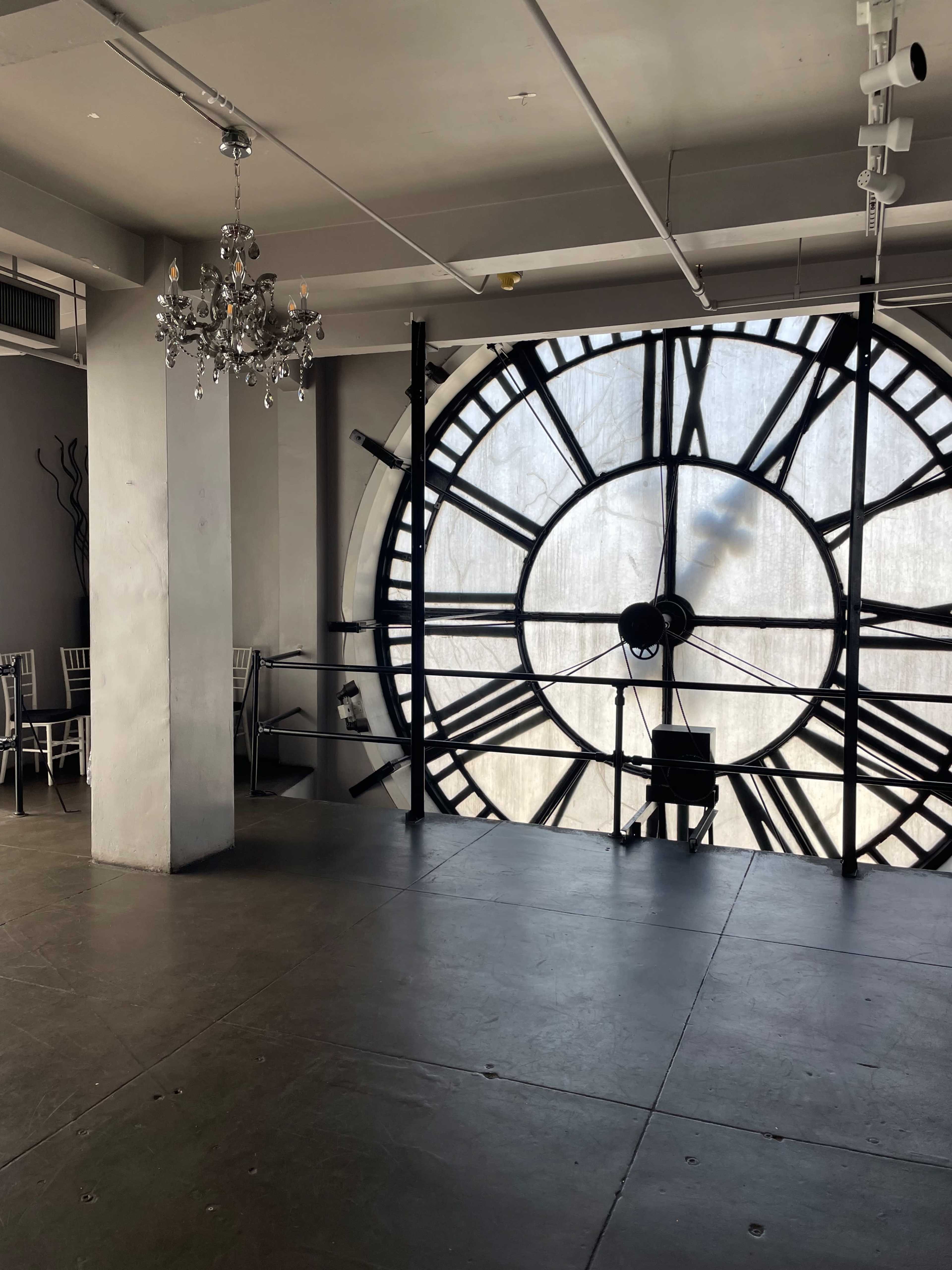 An interior space featuring a large clock face and a chandelier hanging from the ceiling.