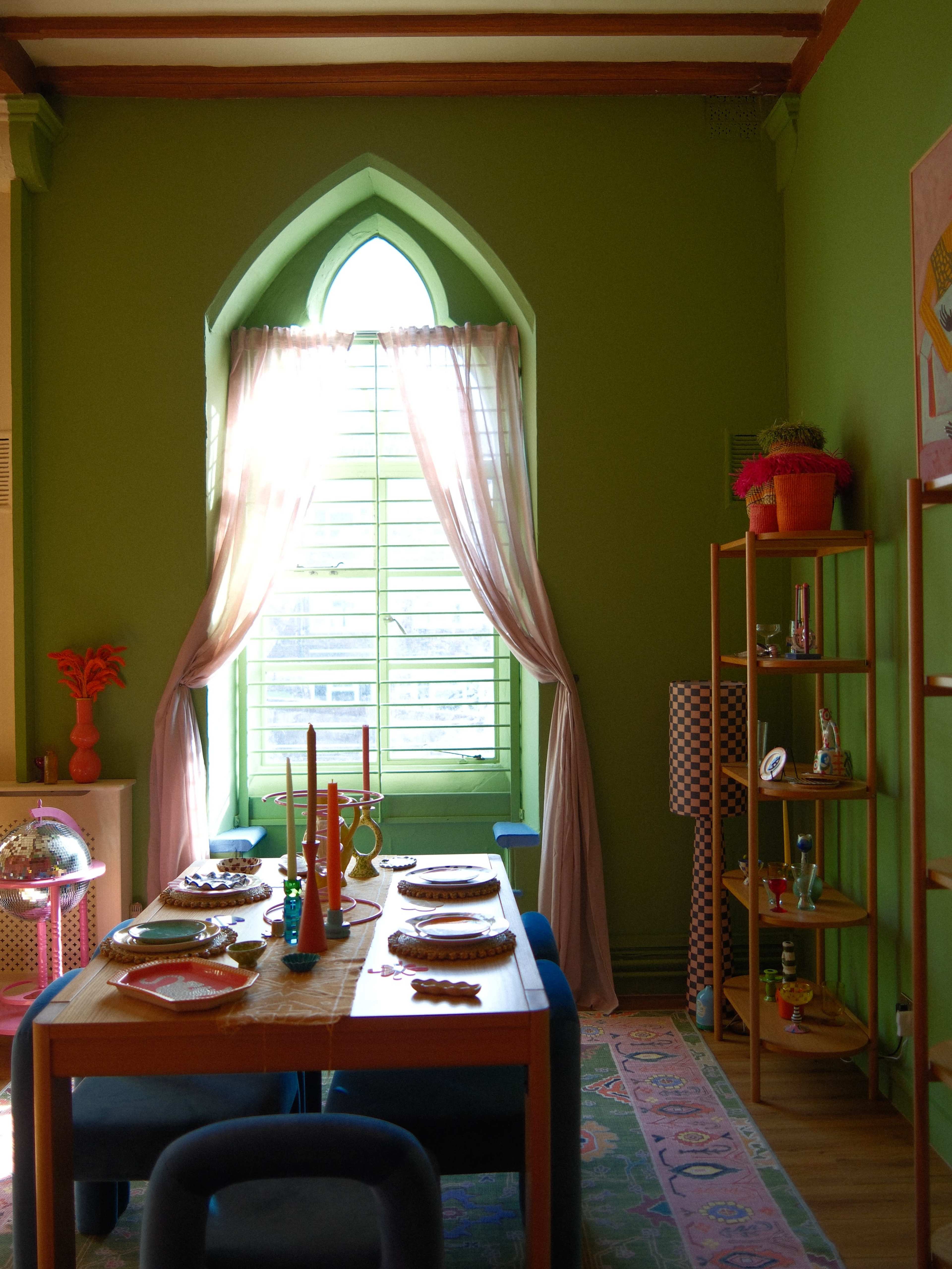 A colorful dining area features a table set for a meal beneath a large arched window with sheer curtains.