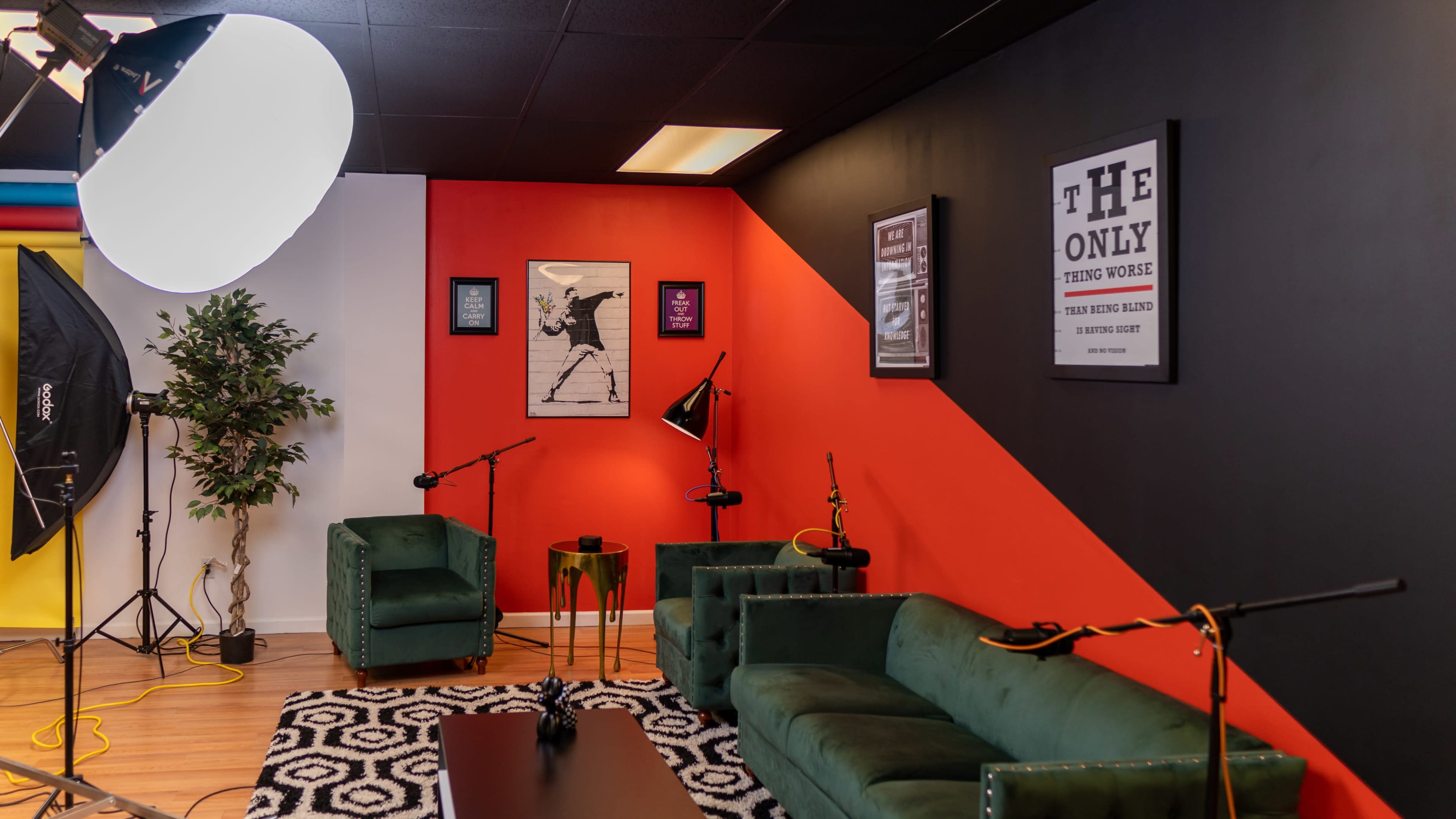 A modern studio space with green velvet furniture, a black and red accent wall, framed artwork, and studio lighting equipment.