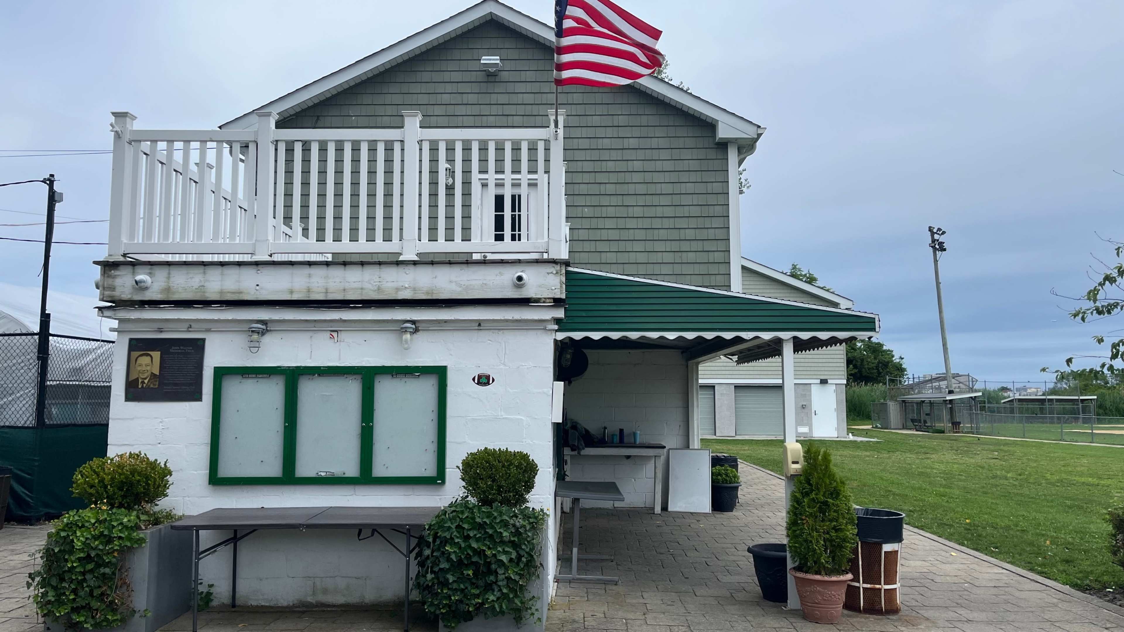 The image shows a two-level building with a green and white striped awning, potted plants in front, and an American flag flying atop the roof.