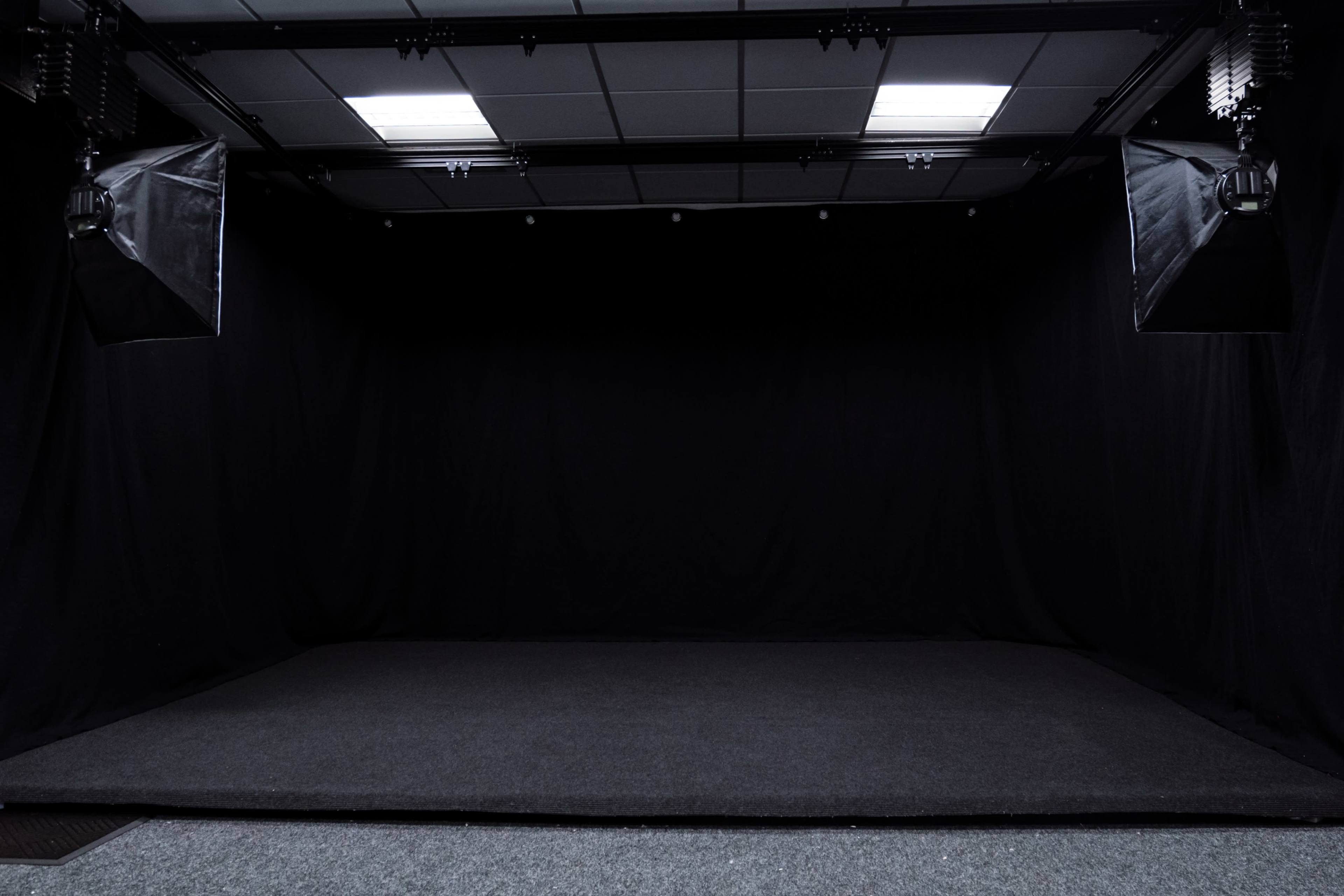 A dark studio space with black curtains and lighting equipment on either side.
