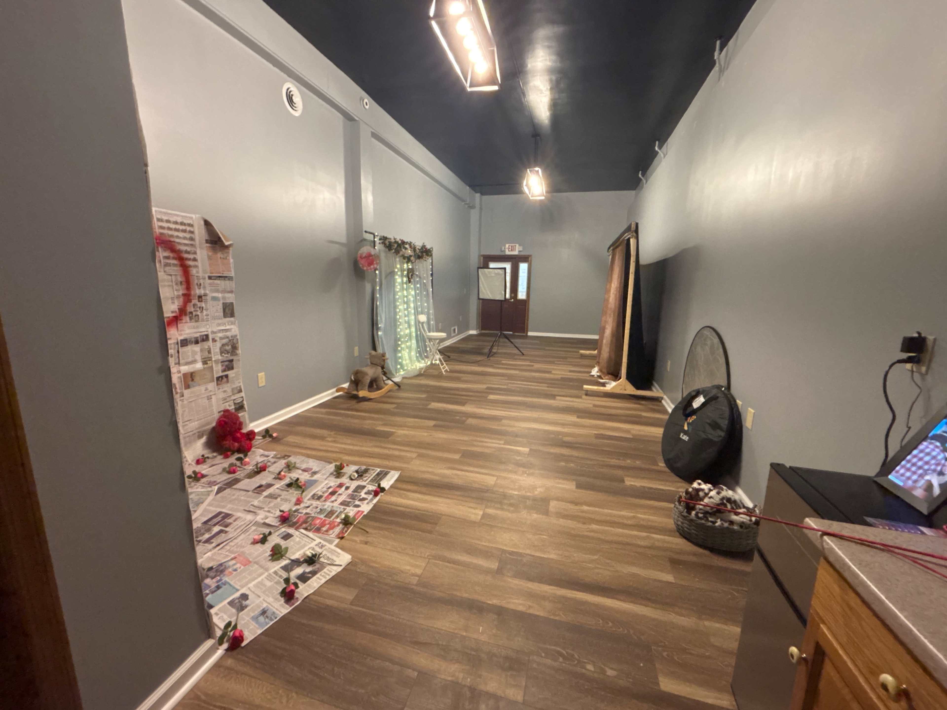 The image shows an empty room featuring wood-like flooring, gray walls, and several decorative elements including a backdrop and props on the floor.