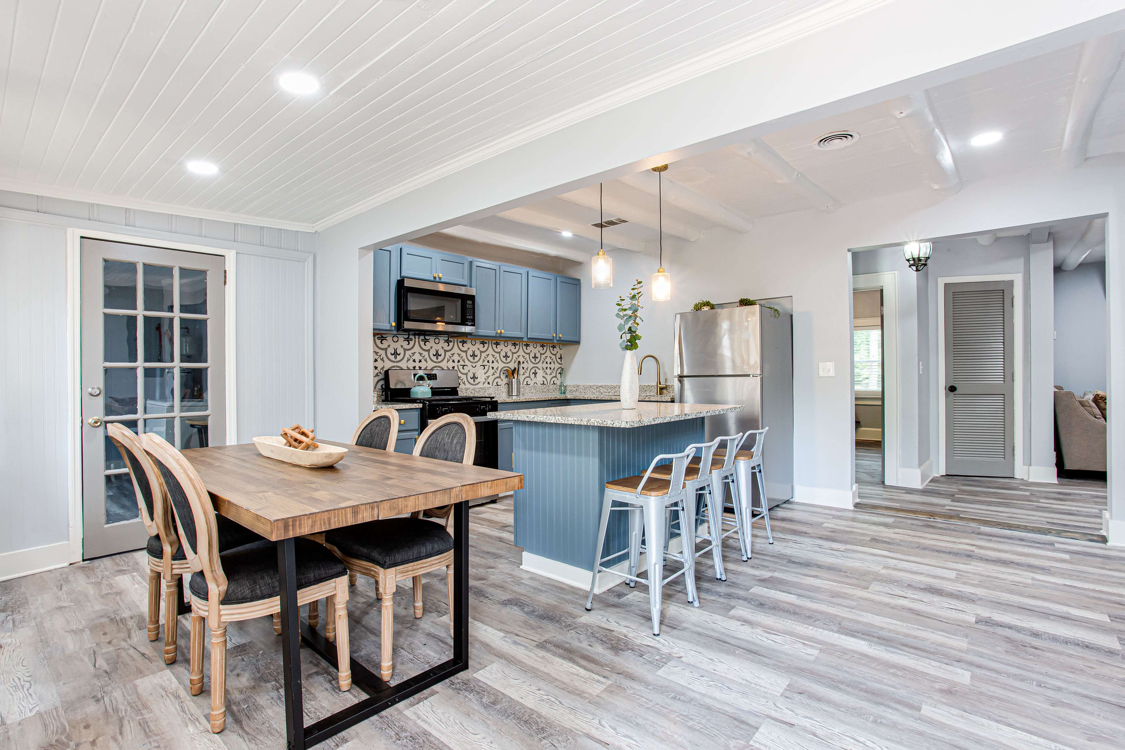 A modern kitchen and dining area features a wooden table with chairs, blue cabinetry, and a sleek countertop with stainless steel appliances.