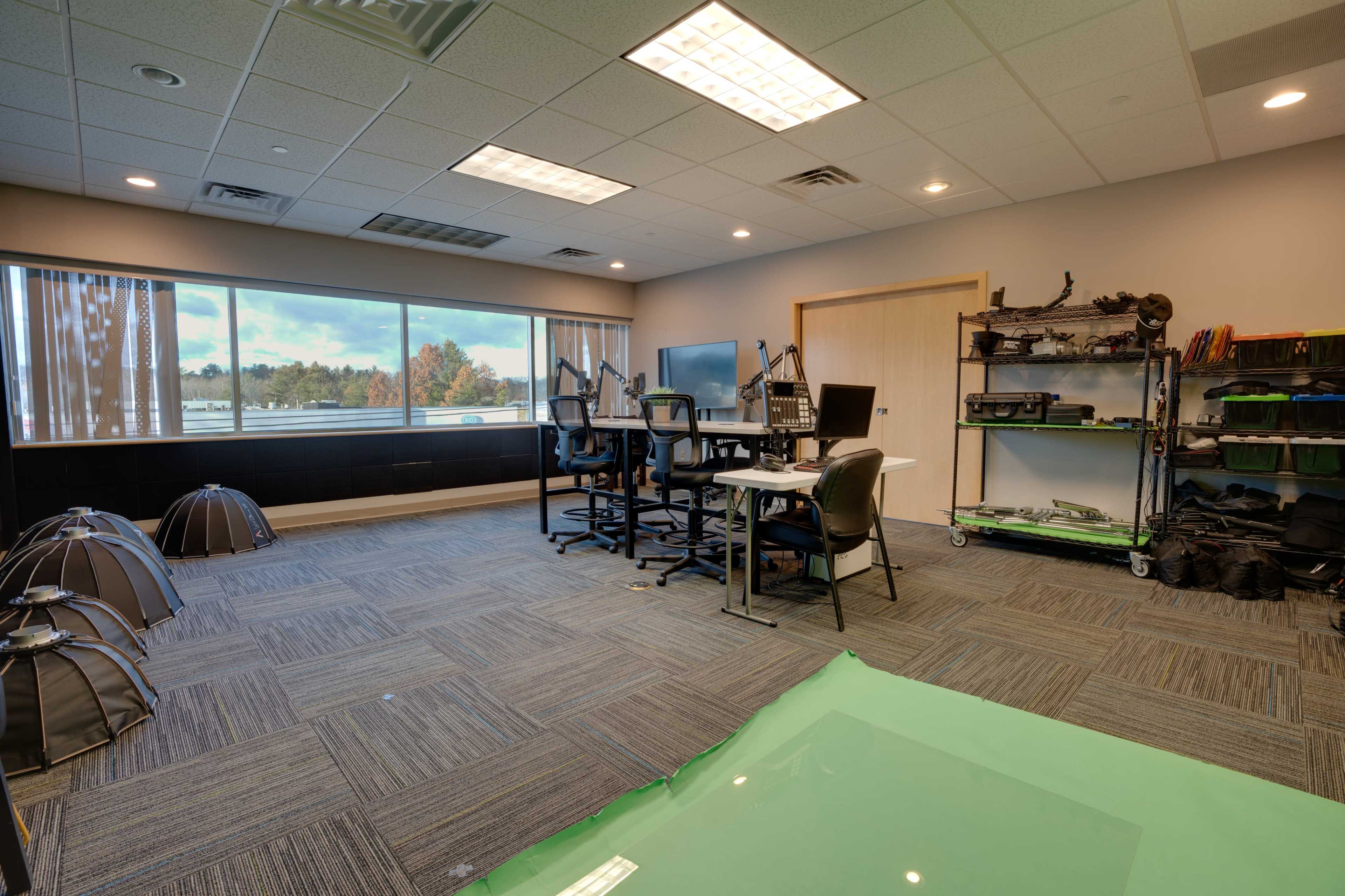 A modern office space featuring several workstations, a large window with a view, and equipment organized on shelves.