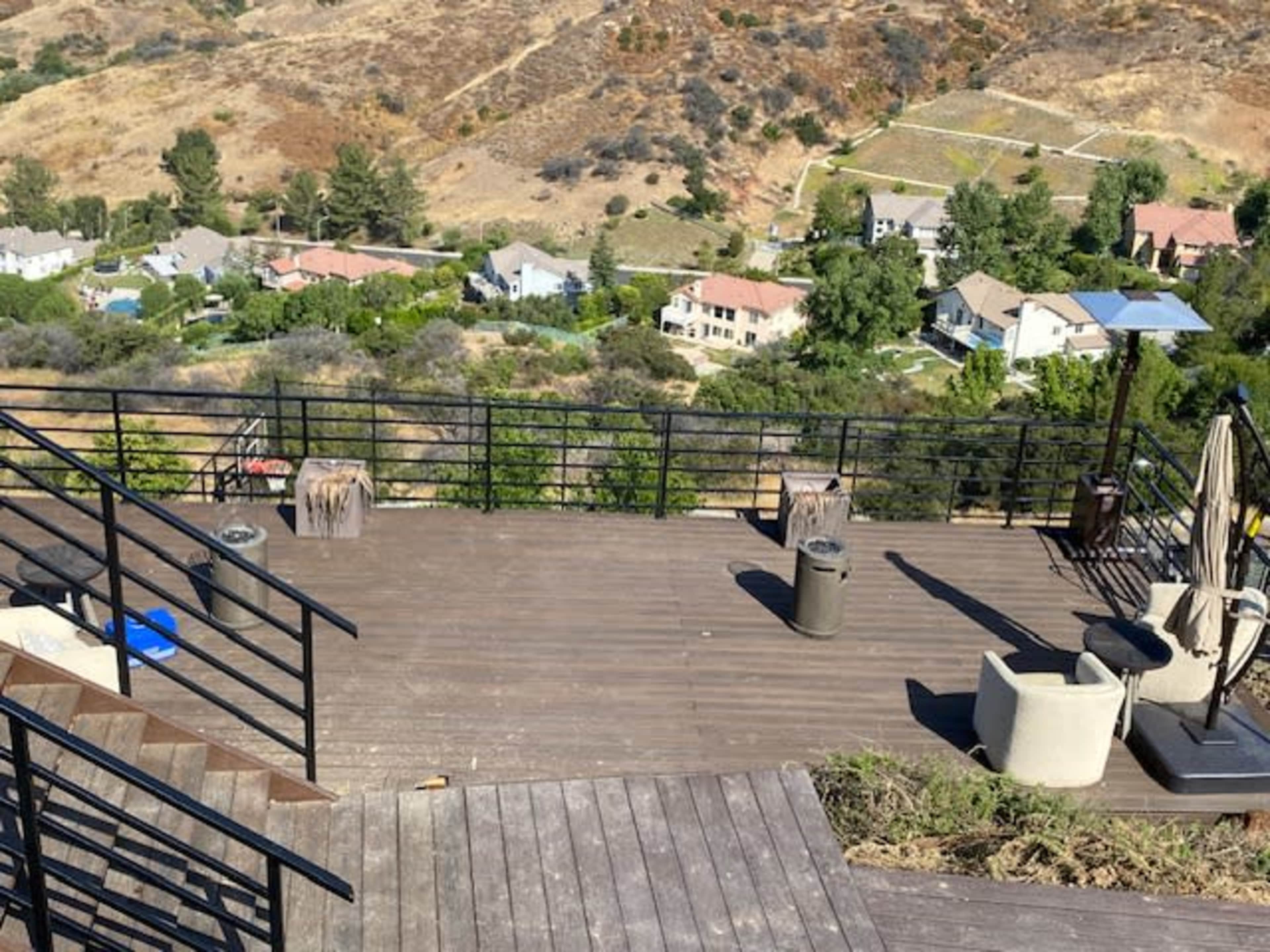 A wooden deck with metal railings overlooks a residential area and hills in the background.