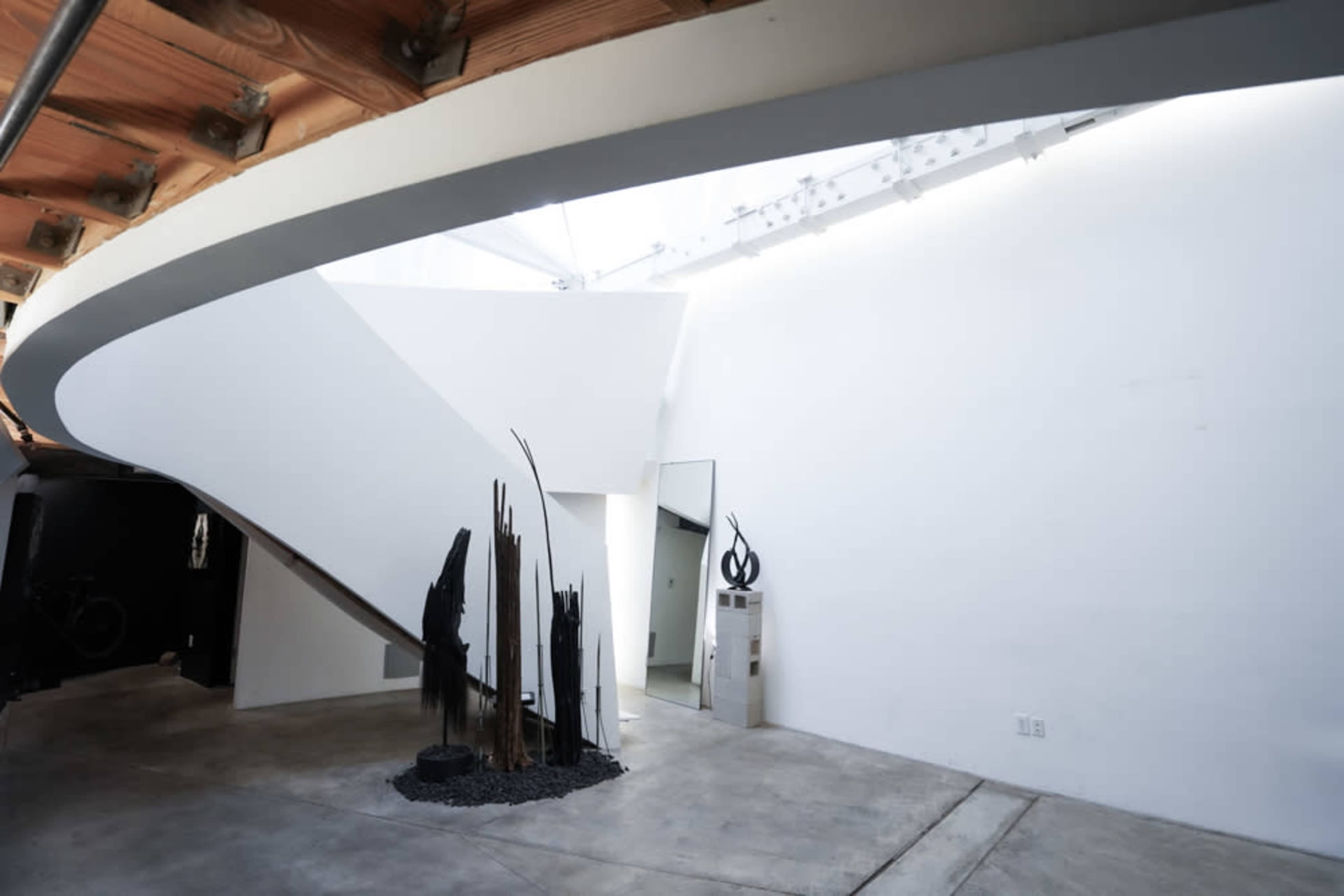 The image shows a modern interior space featuring a curved staircase, minimalist decor, and artistic sculptures against a white wall.