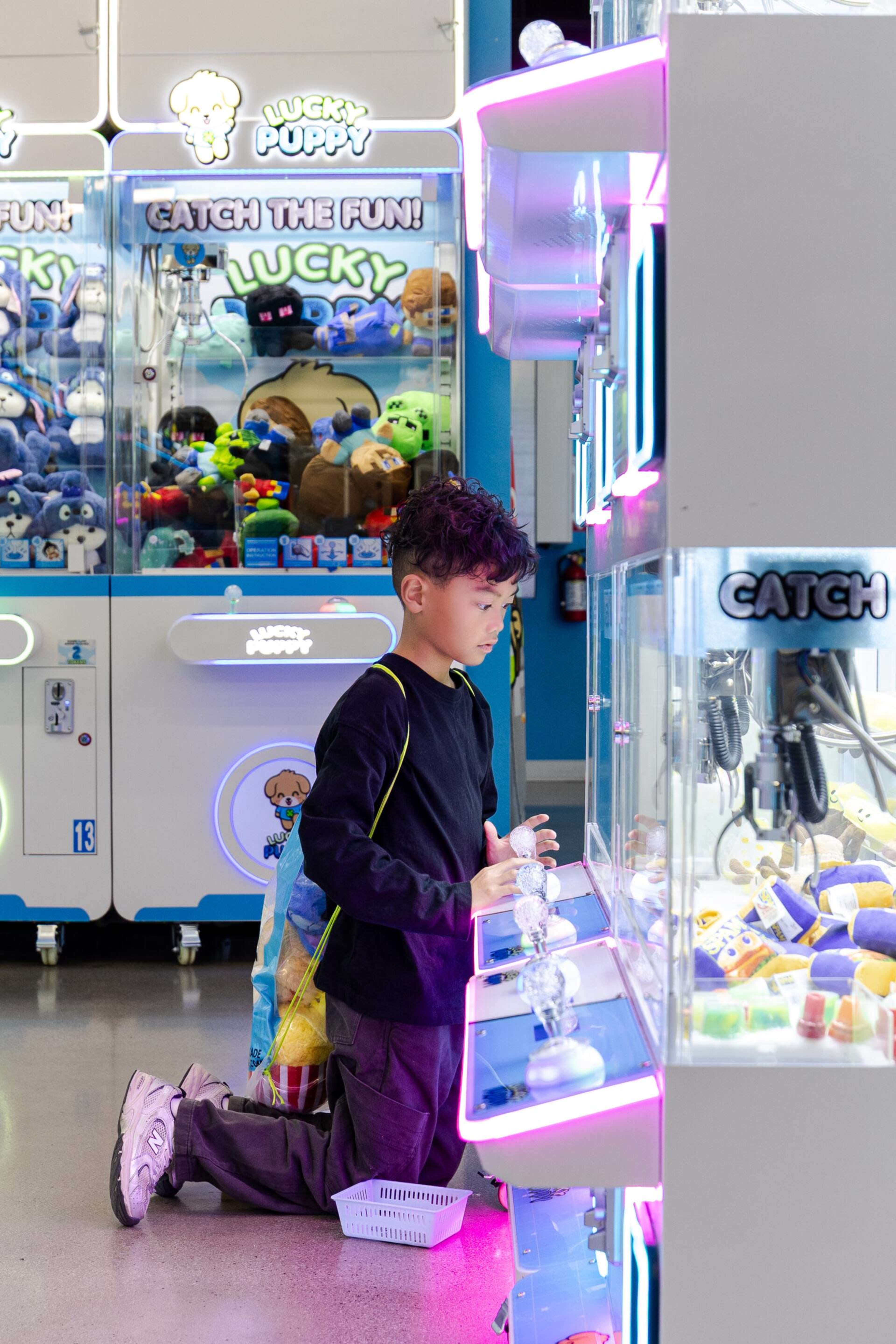 A young child kneels in front of a claw machine, intently focused on attempting to win a plush toy.