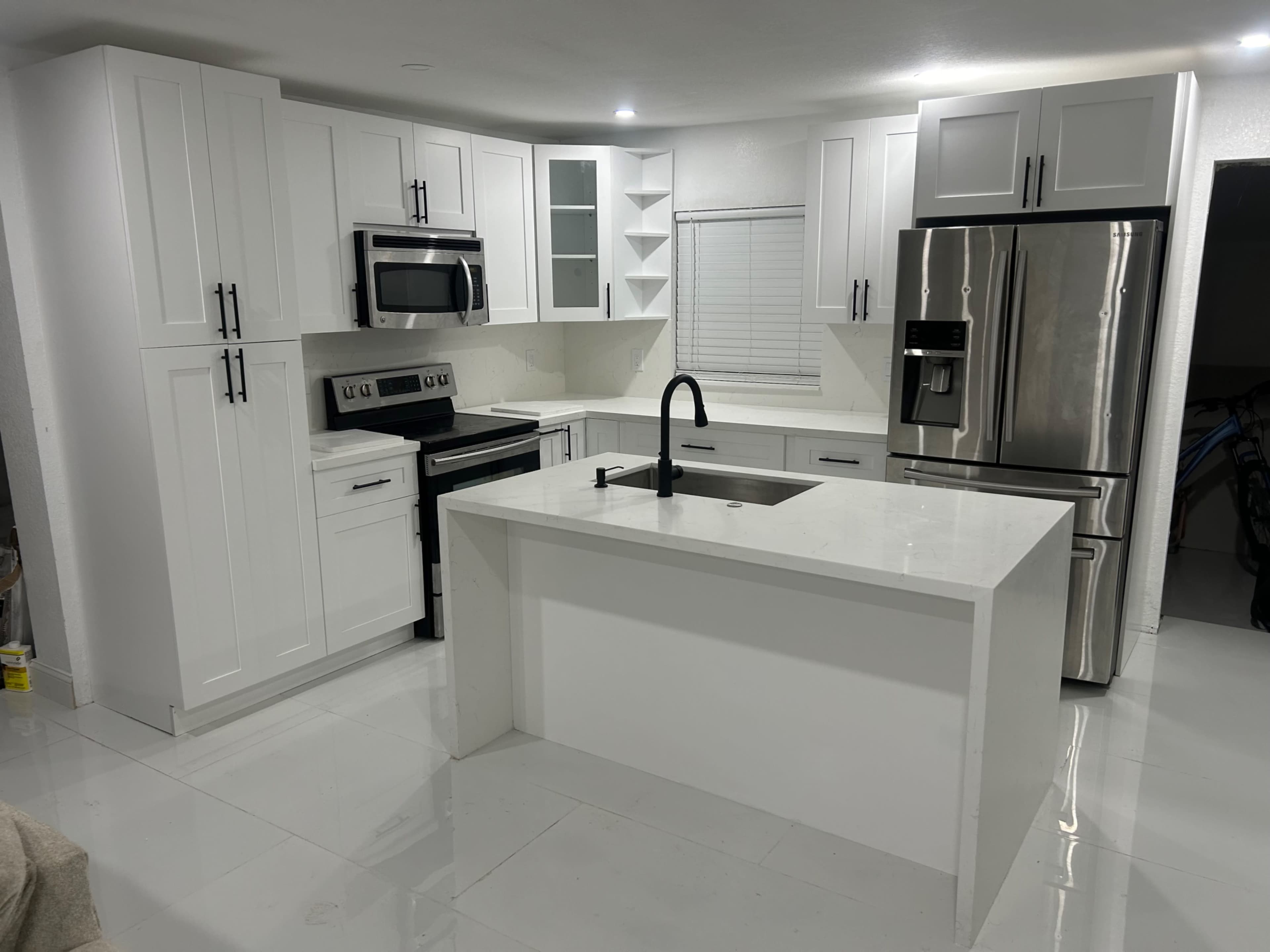 The image shows a modern kitchen with white cabinetry, stainless steel appliances, and a large central island with a sink.