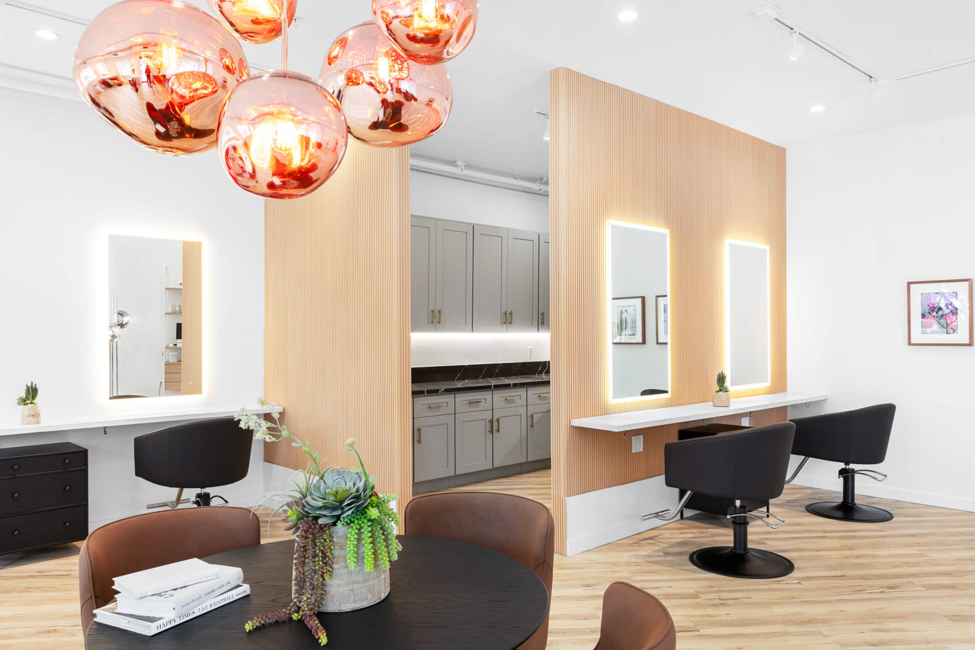 The image shows a modern salon interior featuring a stylish reception area with a round table, black chairs, and illuminated mirrors along a wooden partition.