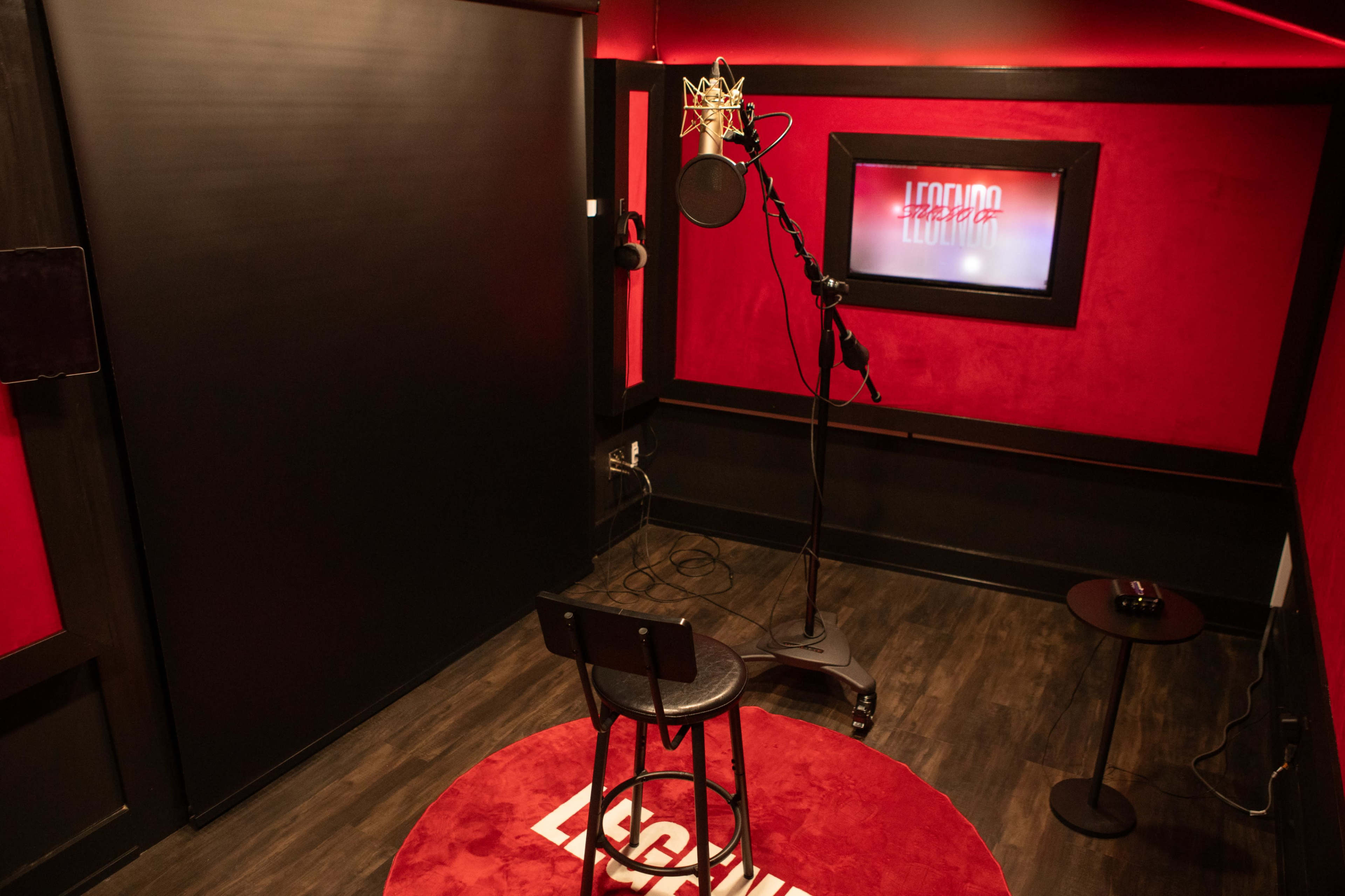 A small soundproof recording studio featuring a microphone on a stand, a black stool, and red-accented walls.