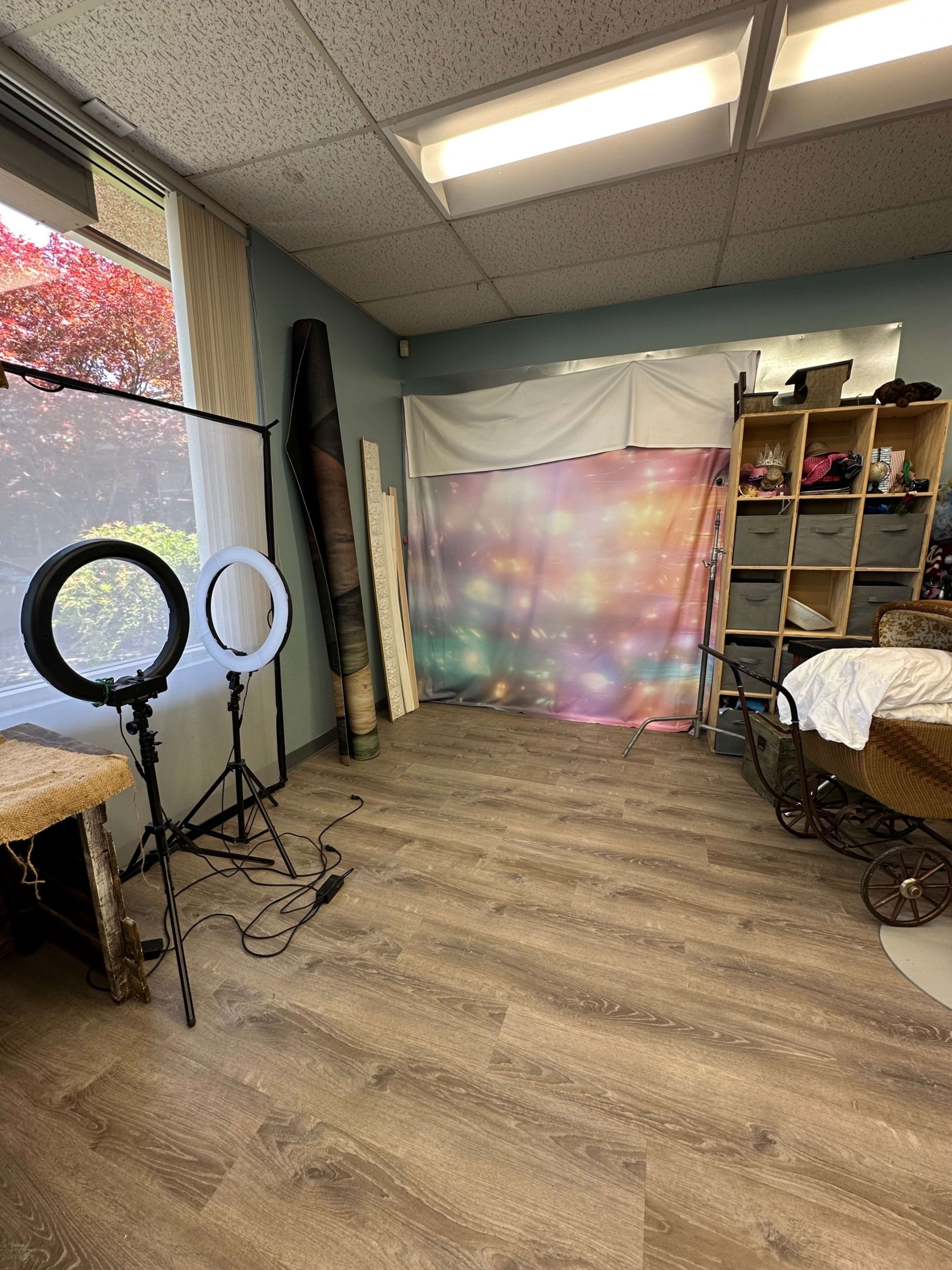 The image shows a spacious room with a colorful backdrop, two circular light stands, and a shelf filled with various items.
