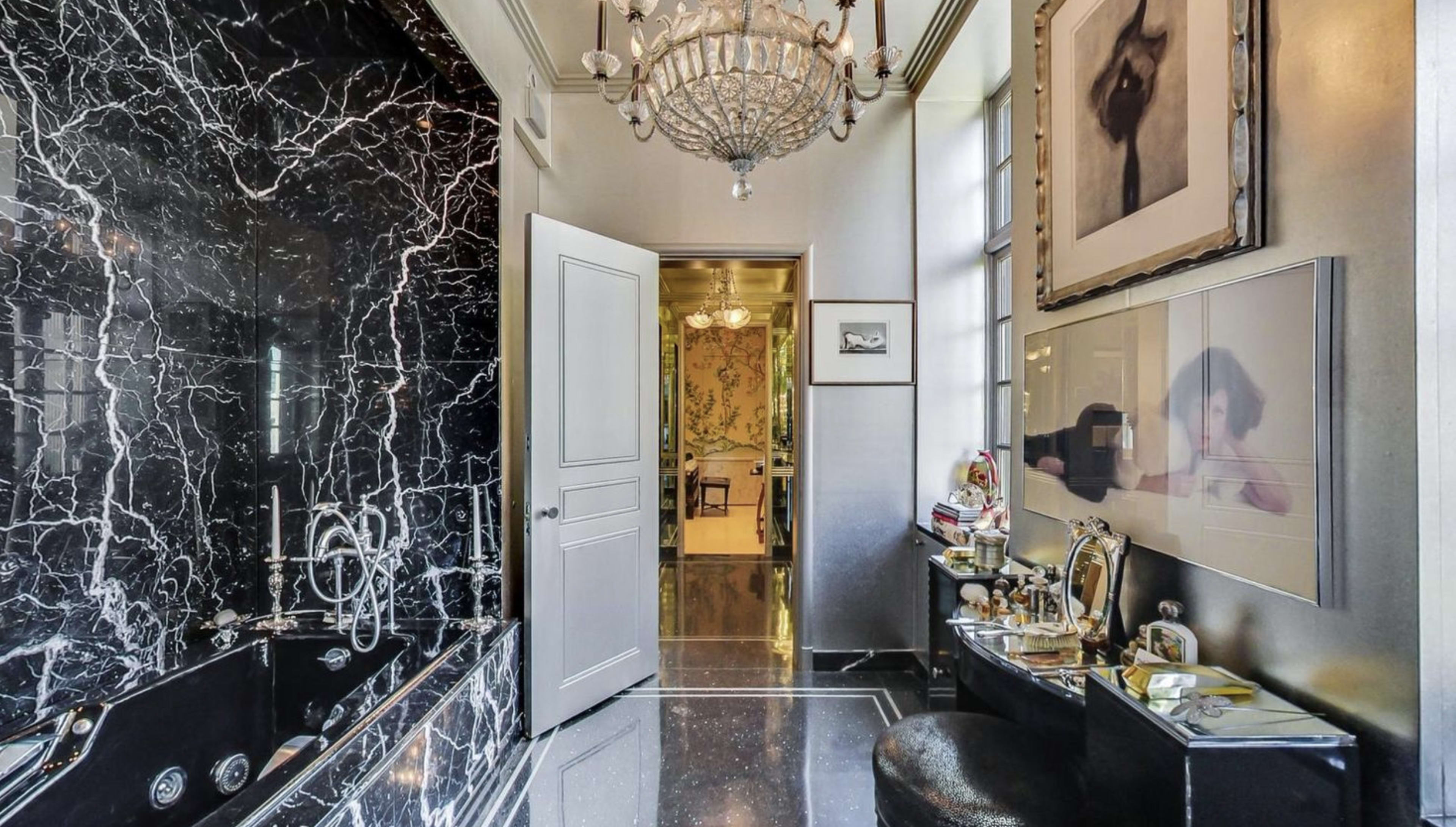 A luxurious bathroom featuring black marble walls, a chandelier, and a doorway leading to an adjoining room.