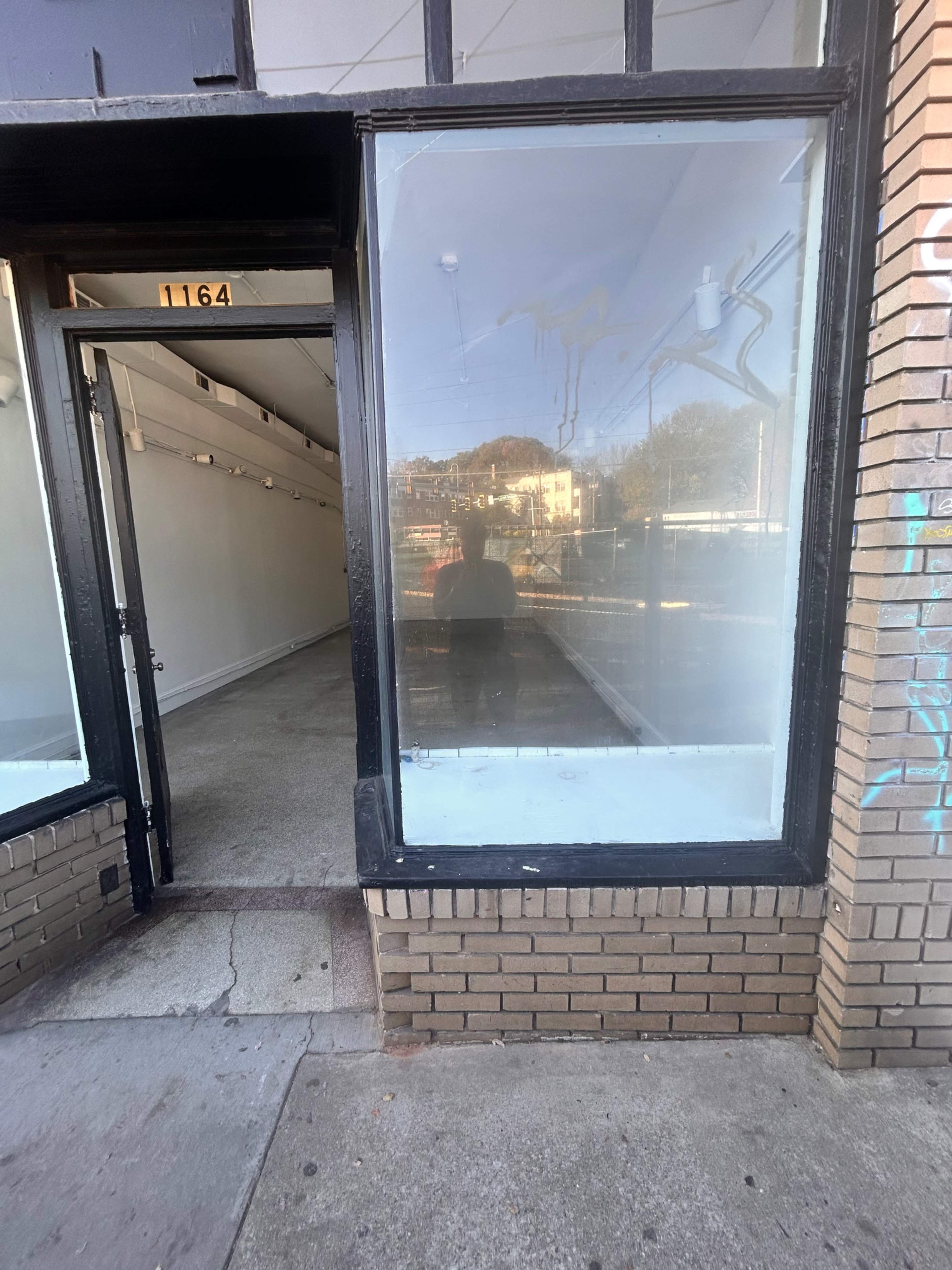 The image shows an empty storefront with large windows and a brick facade, revealing a barren interior space.