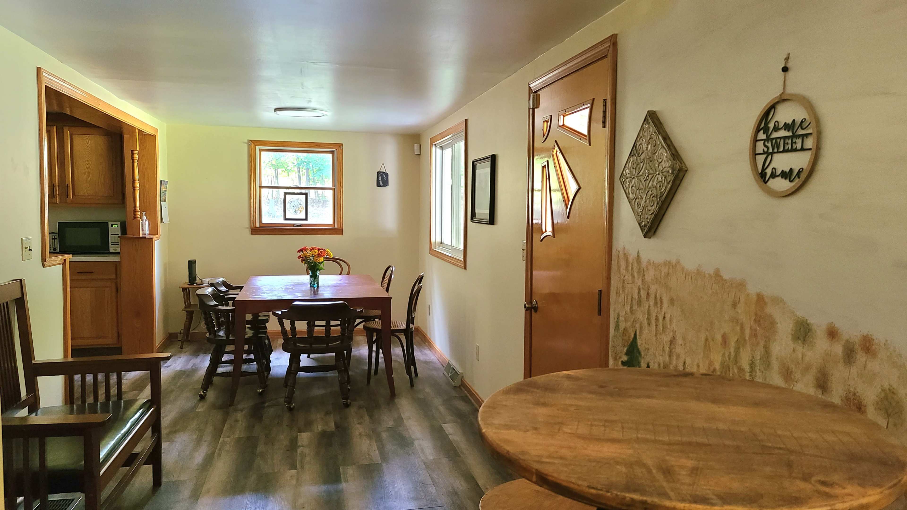 A bright room with a wooden dining table and chairs, a small kitchen area, and a door leading outside.