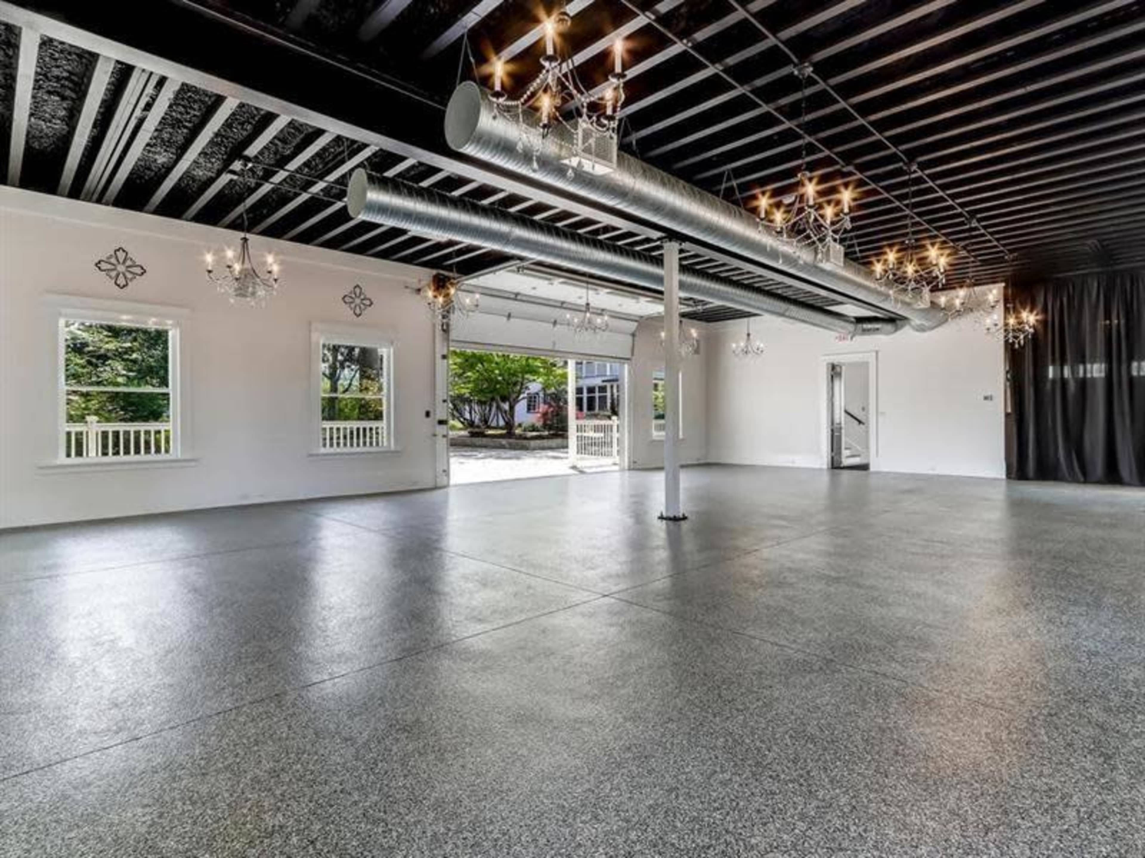 The image shows a spacious, empty room with polished concrete floors, large windows, and several decorative chandeliers hanging from the ceiling.