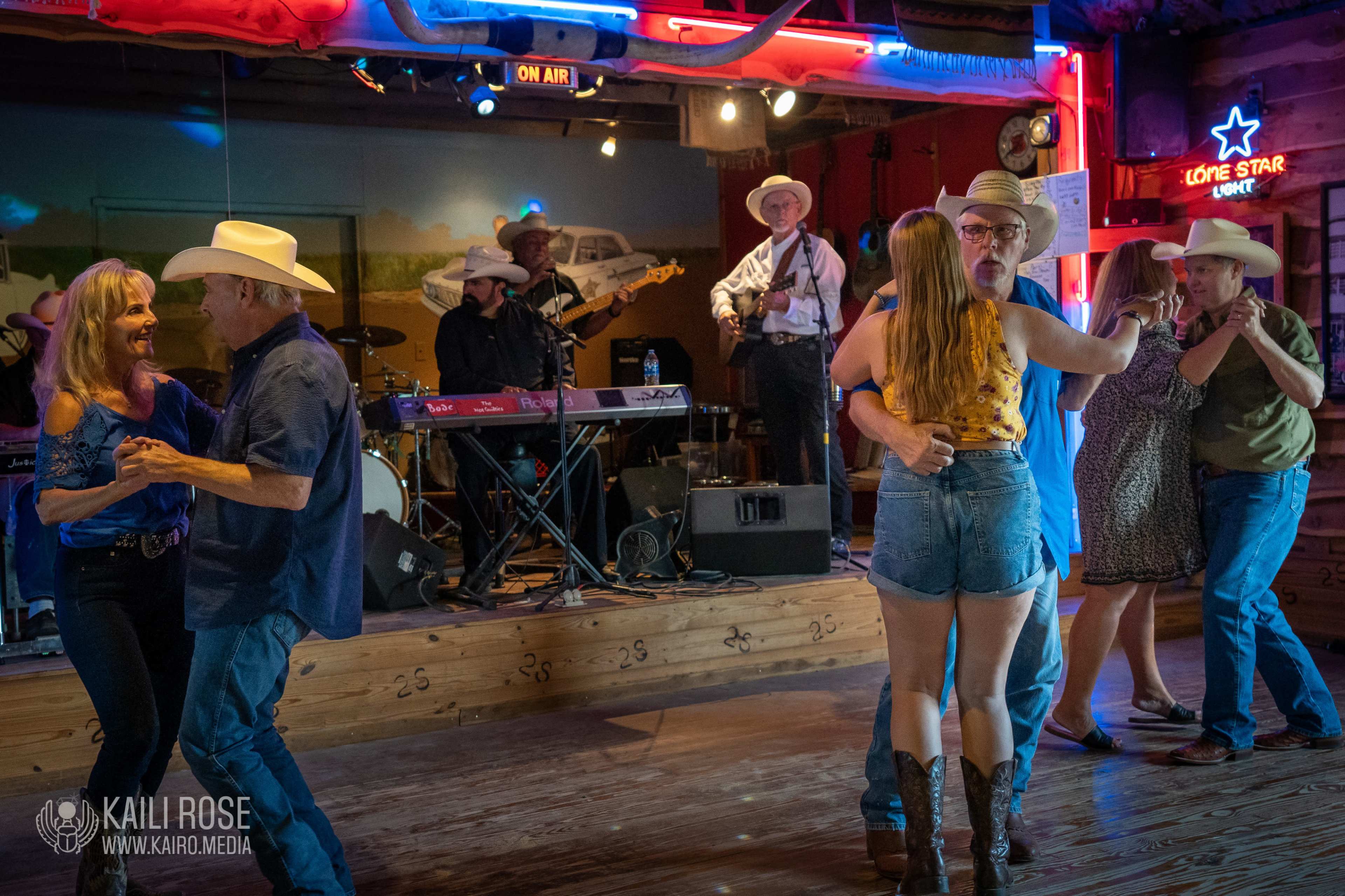 A group of people dance in a spacious venue with a live band performing in the background.