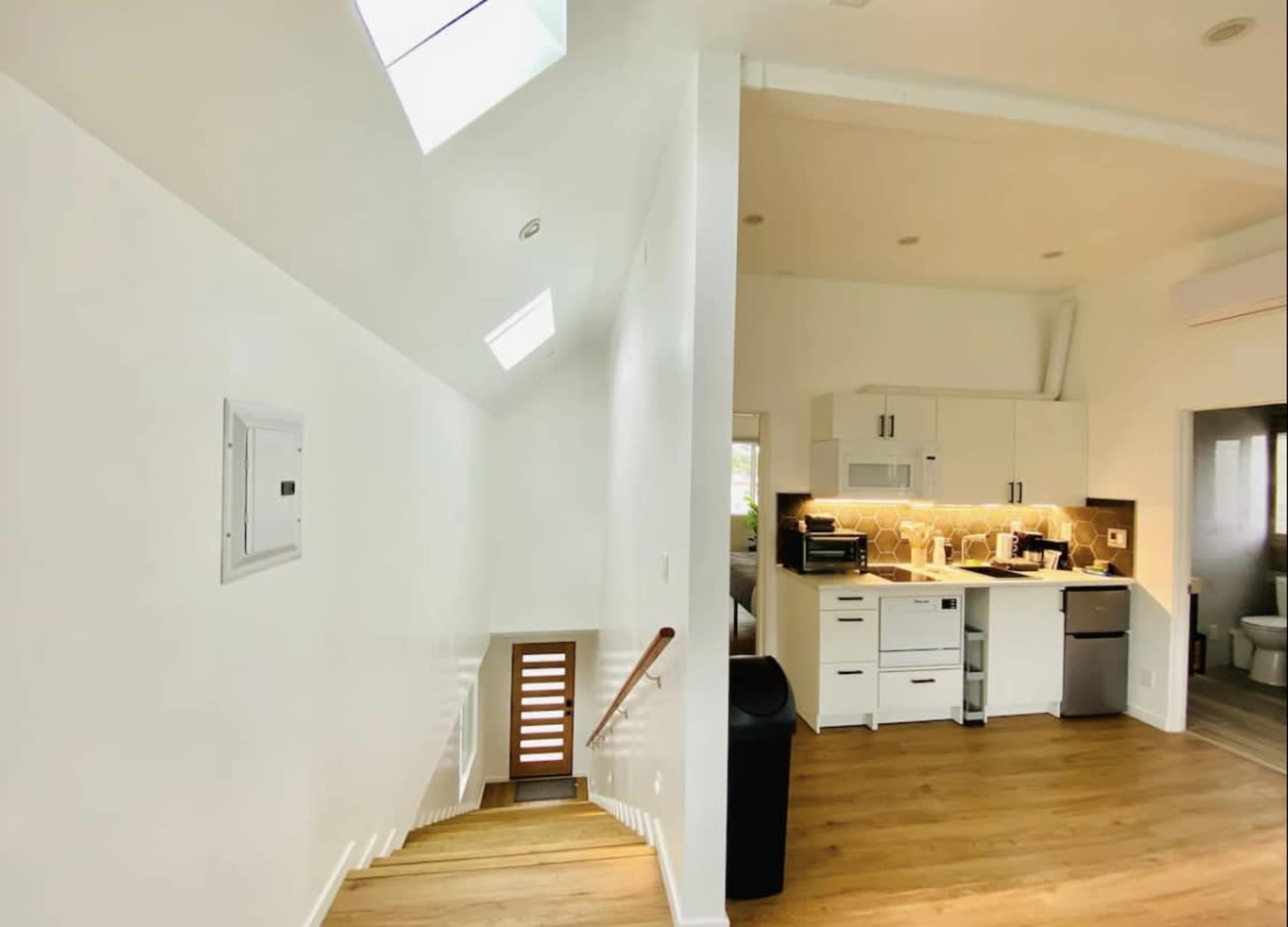 A modern interior space with a staircase leading down on the left, and a kitchen area with white cabinetry and appliances on the right.
