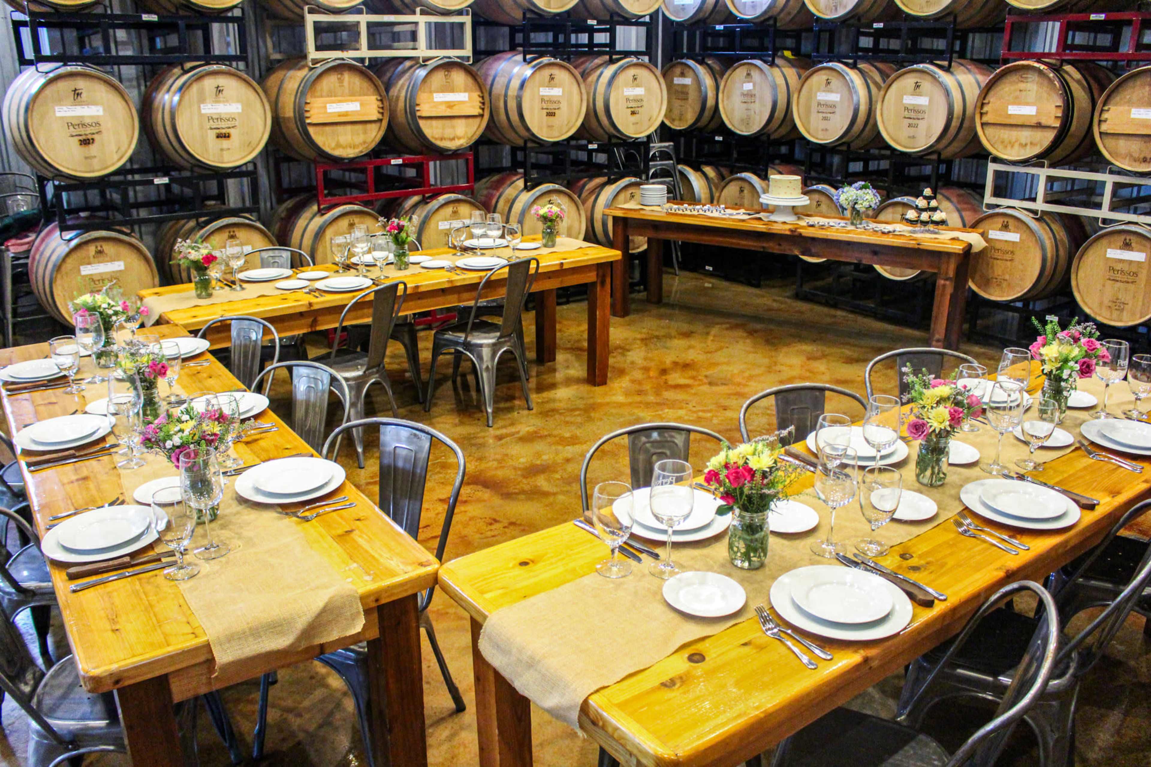 A dining area is set with wooden tables and metal chairs, surrounded by wine barrels.