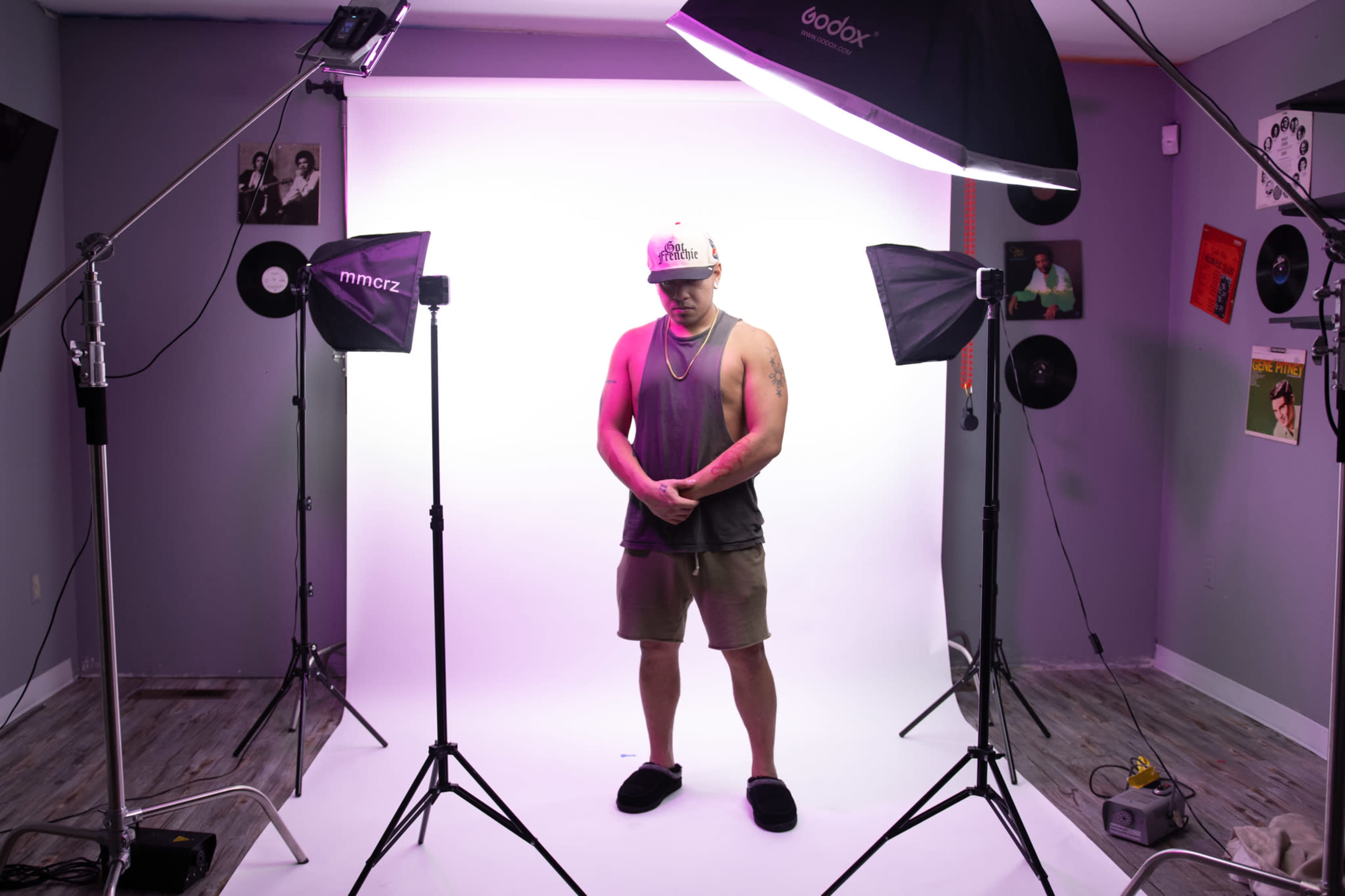 A person stands in the center of a photo studio, surrounded by professional lighting equipment and a blank backdrop.
