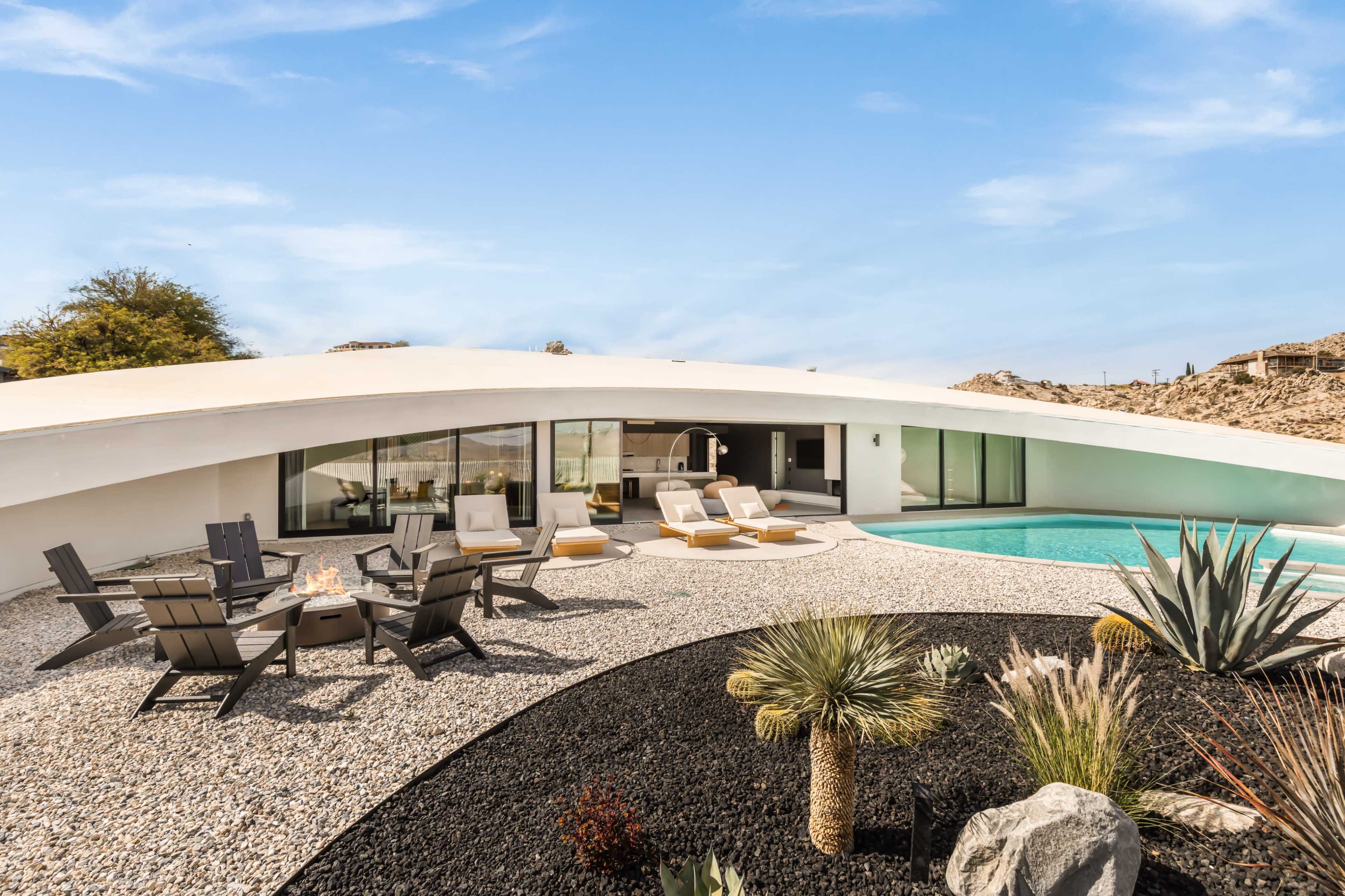 The image shows a modern curved-roof house with a swimming pool, surrounded by landscaped gravel and decorative plants.