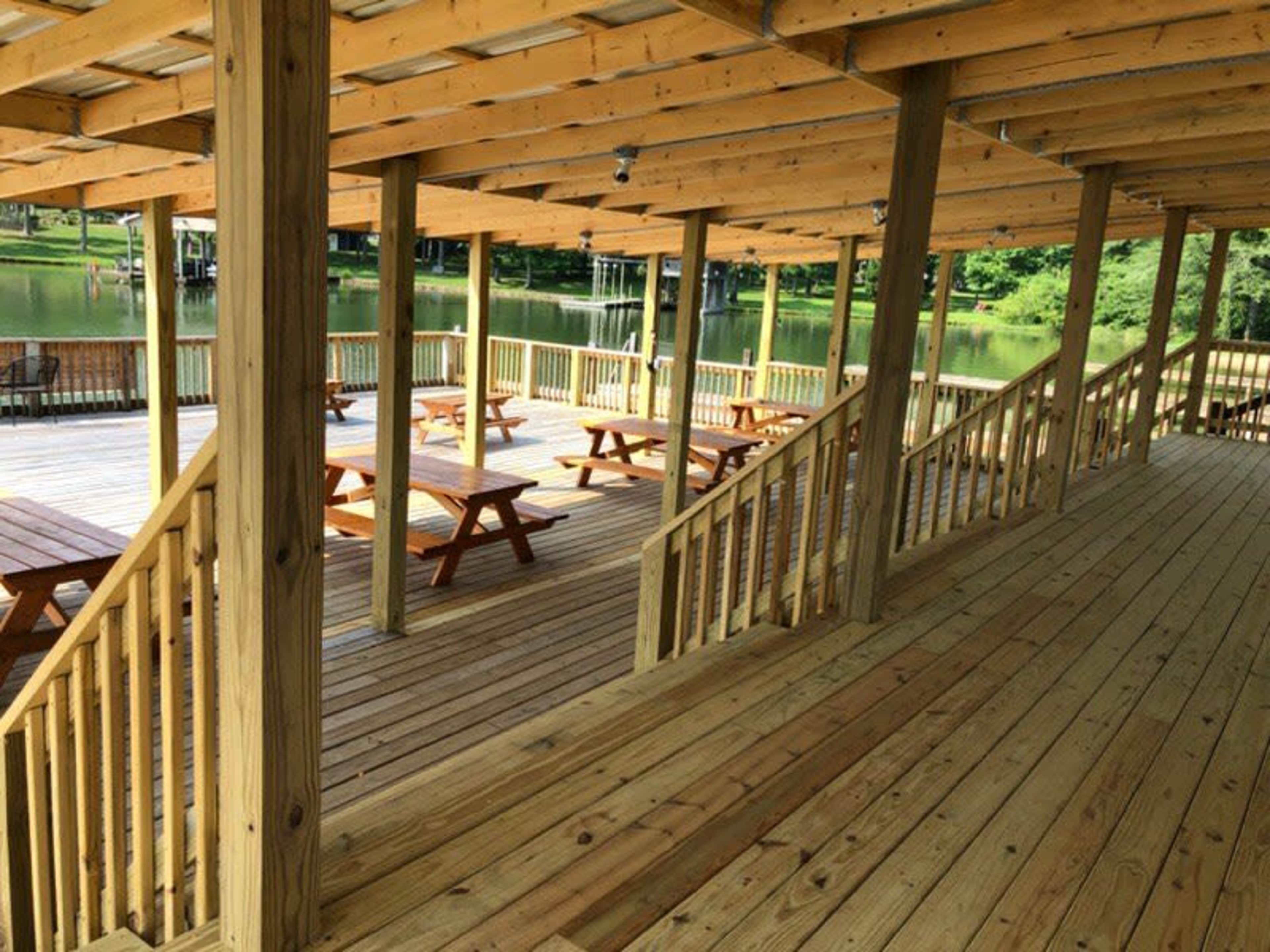A wooden pavilion with picnic tables and stairs, overlooking a body of water.