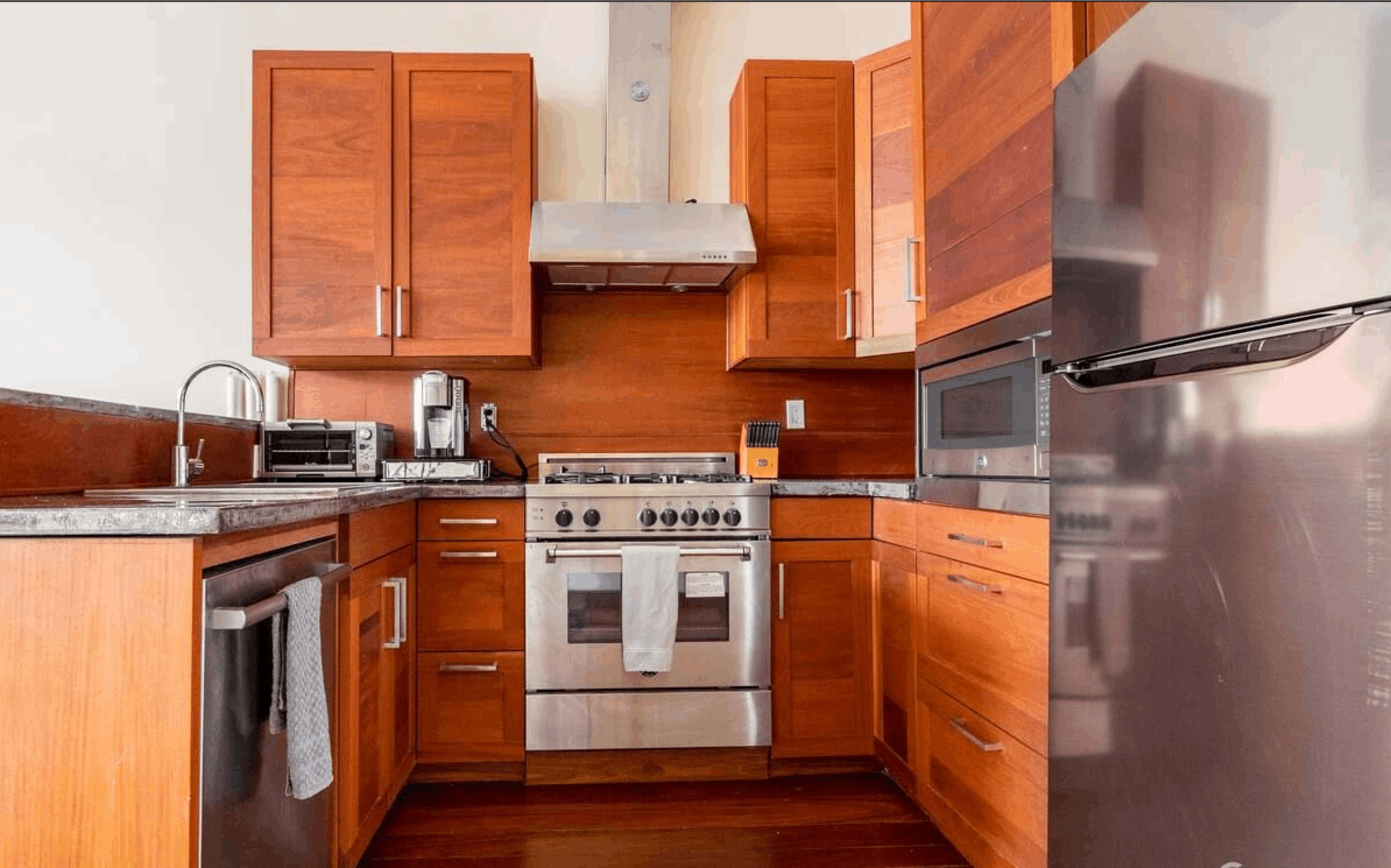 A modern kitchen with wooden cabinets, stainless steel appliances, and a granite countertop.