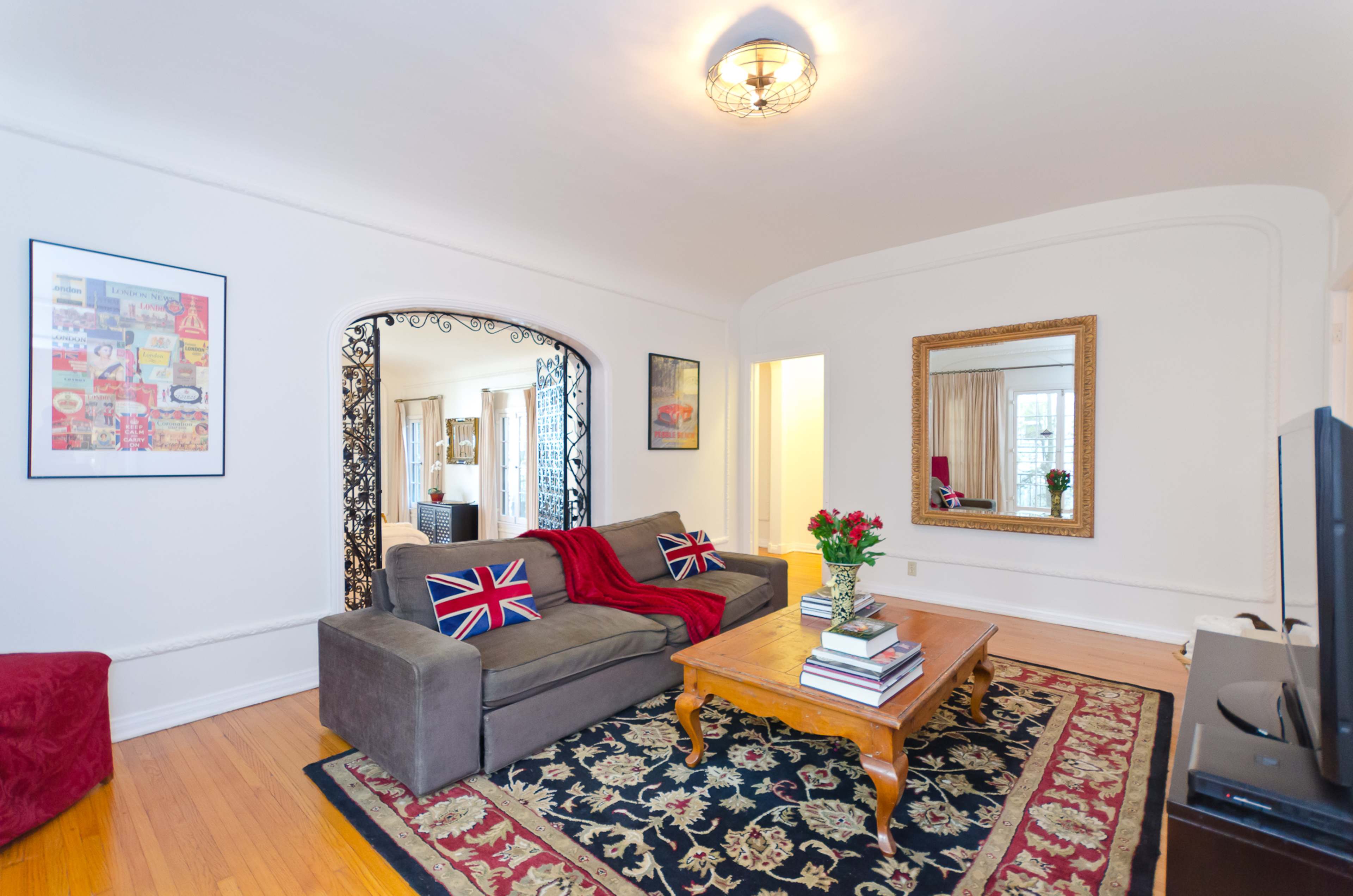 The living room features a gray sofa with a Union Jack throw pillow, a wooden coffee table, and large windows surrounded by decorative curtains.