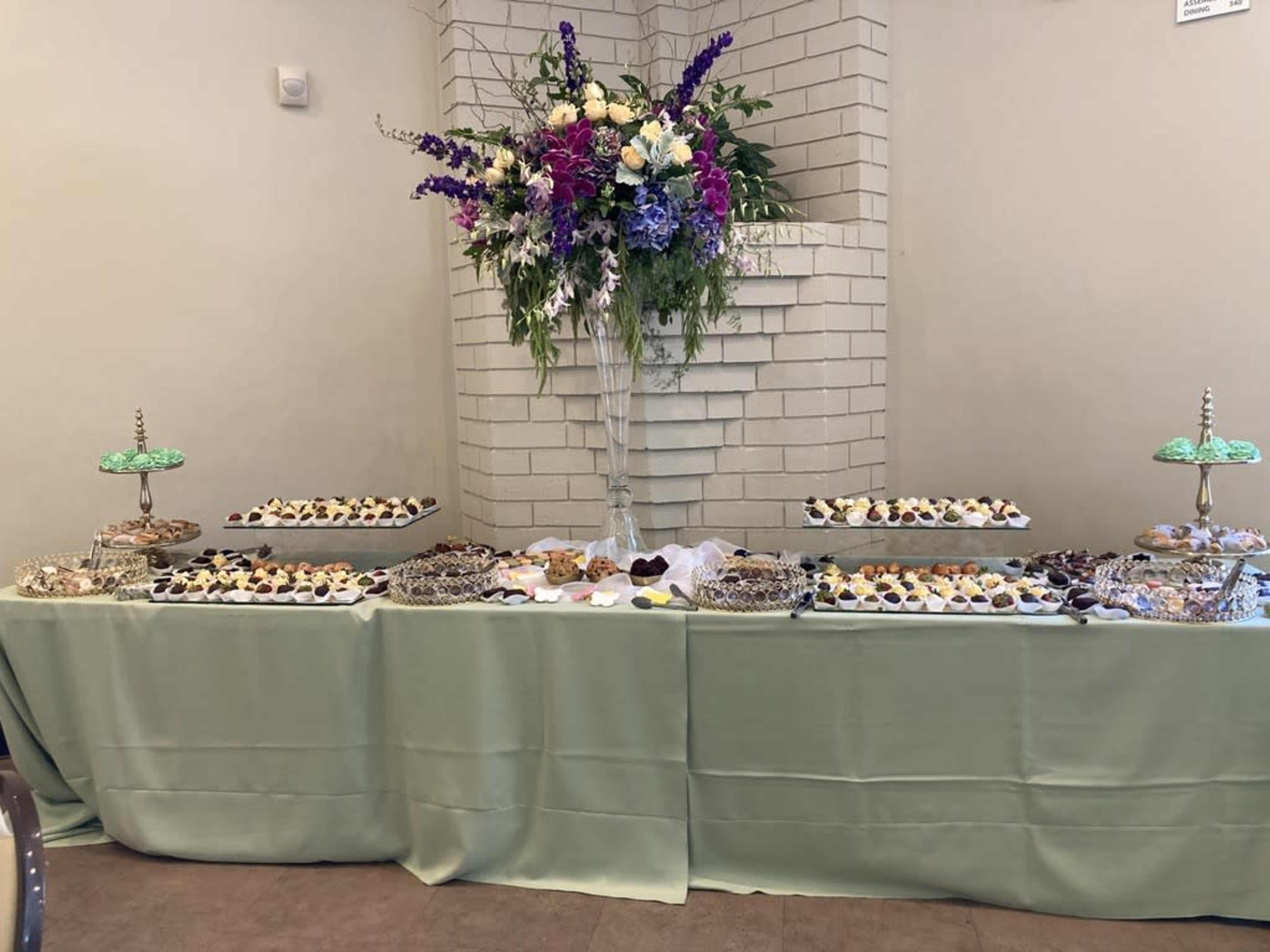 A decorative table displays an assortment of pastries and desserts, with a large floral arrangement in the center.